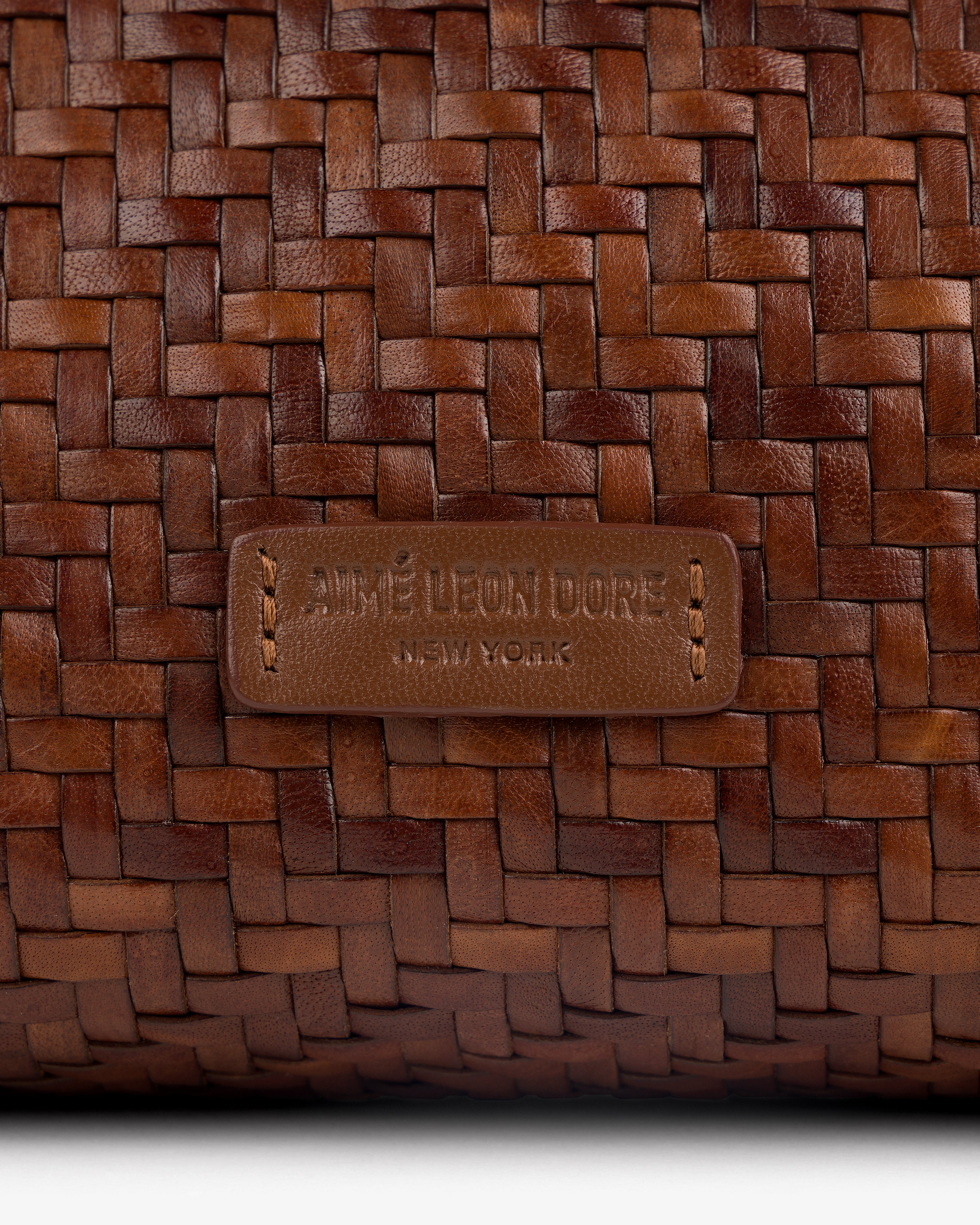 Close-up of a brown Woven Leather Shoulder Bag with an AIMÉ LEON DORE NEW YORK label stitched on the front.