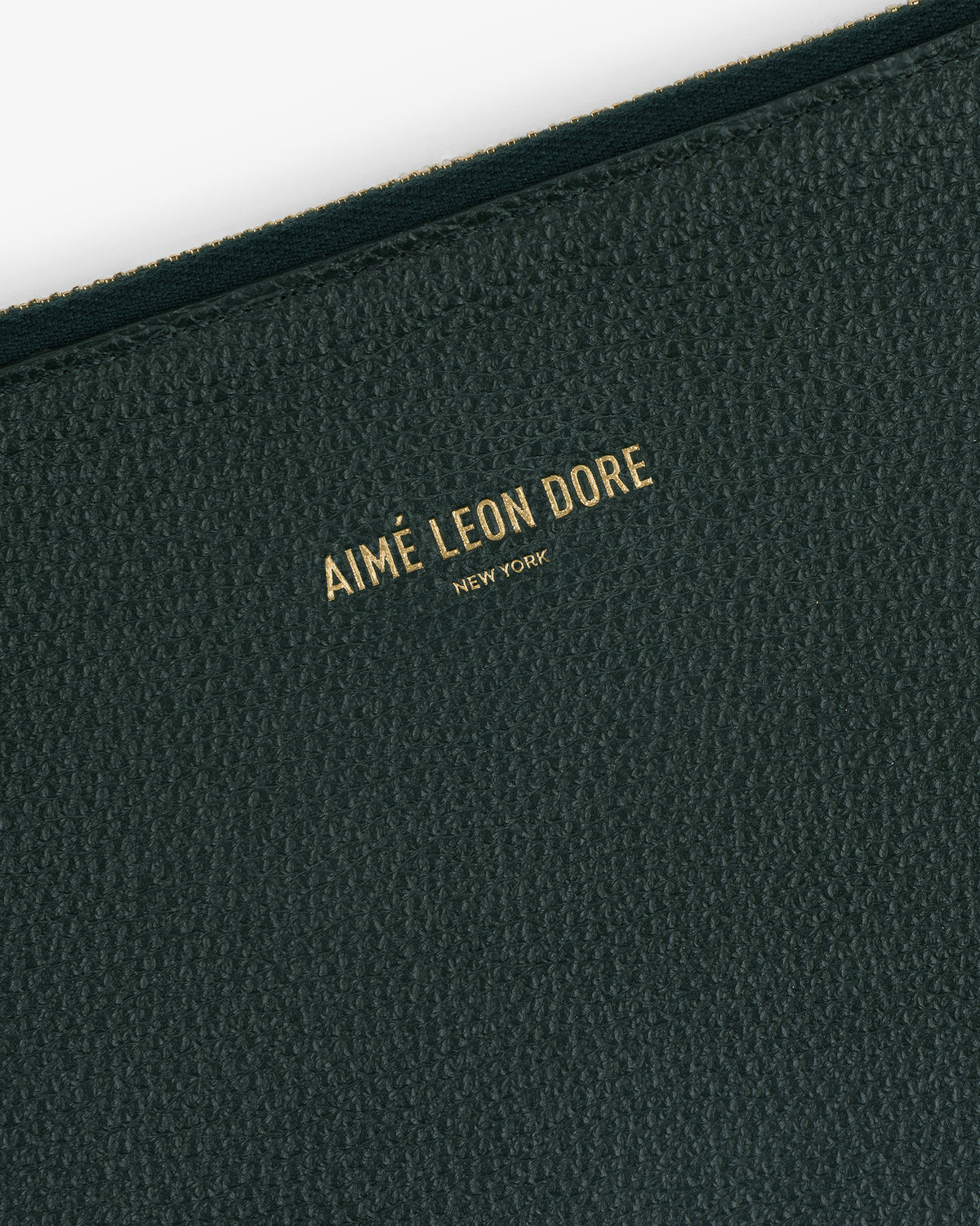 Close-up of a textured dark green Large Leather Pouch with AIMÉ LEON DORE NEW YORK embossed in gold letters.