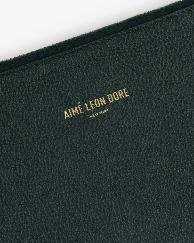 Close-up of a textured dark green Large Leather Pouch with AIMÉ LEON DORE NEW YORK embossed in gold letters.