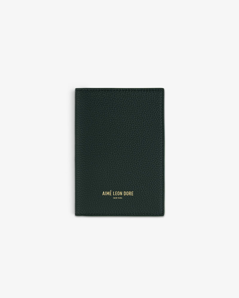 Dark green leather passport holder with AIMÉ LEON DORE NEW YORK embossed in gold on the front, centered on white.
