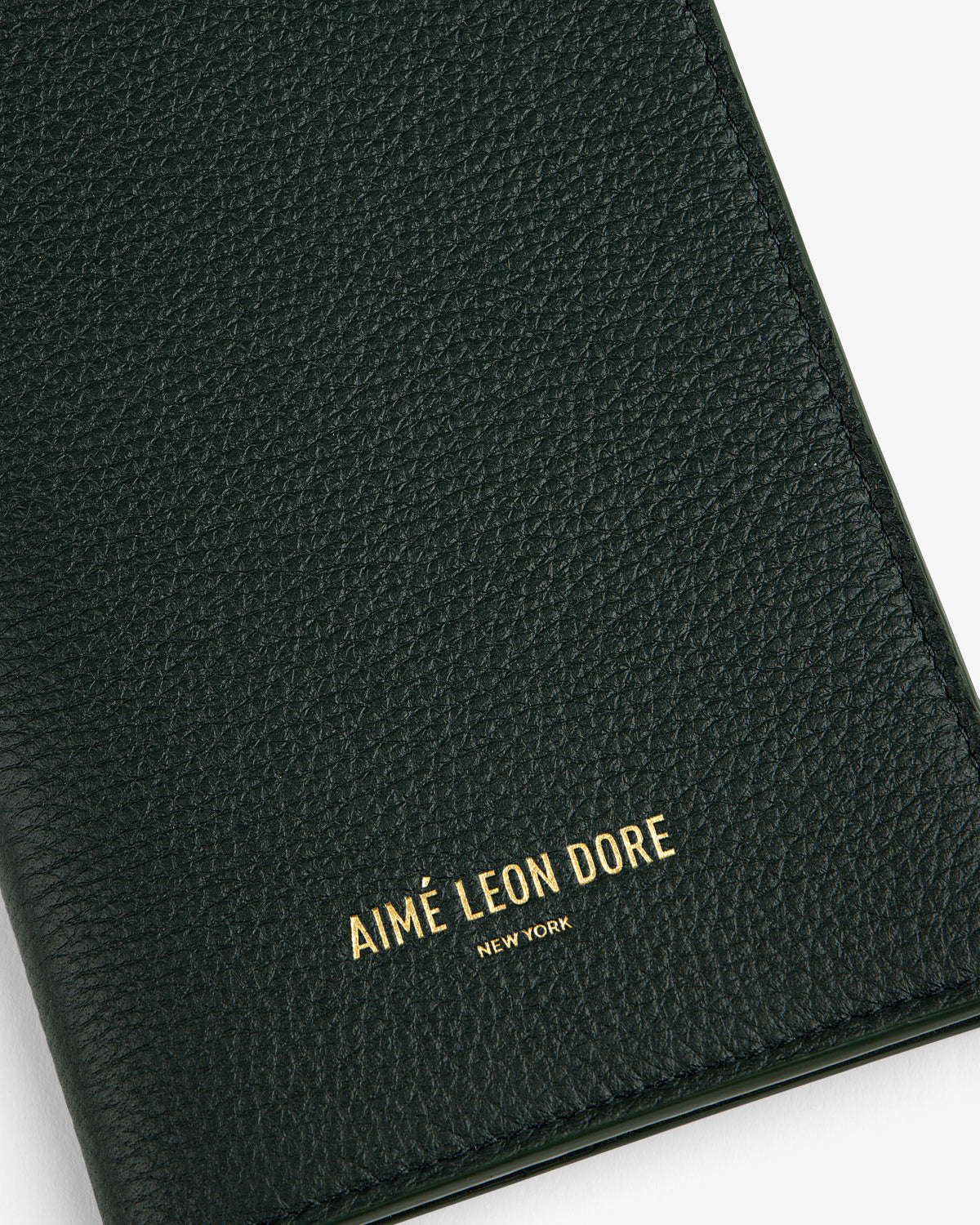 Close-up of a textured dark green Leather Passport Holder with AIMÉ LEON DORE NEW YORK embossed in gold.