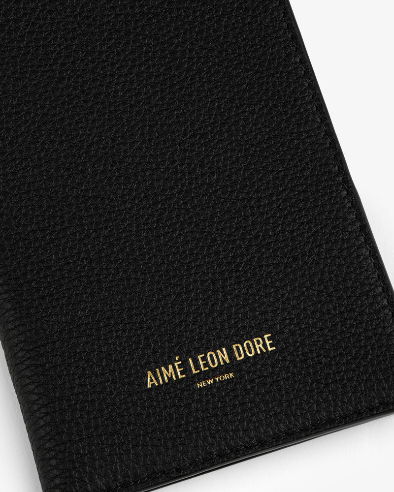 Black textured leather passport holder with AIMÉ LEON DORE NEW YORK embossed in gold at the bottom.