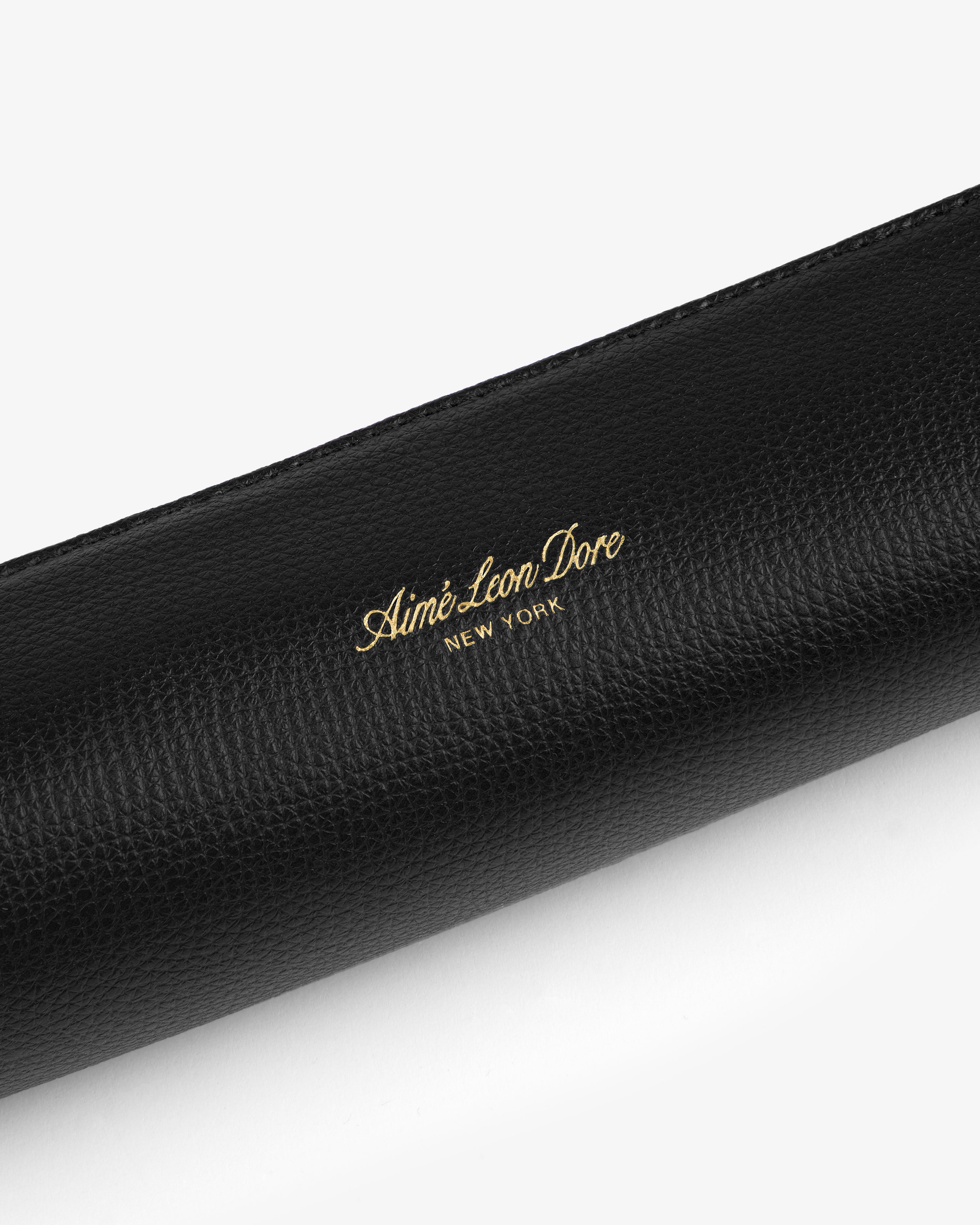 Black leather pencil case with gold Aimé Leon Dore New York branding embossed on its textured surface.