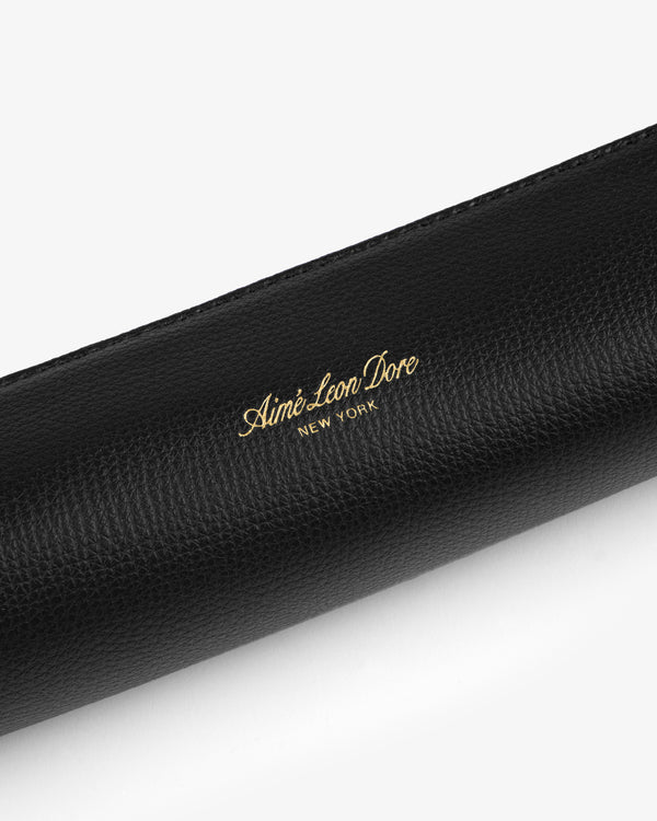 Black leather pencil case with gold Aimé Leon Dore New York branding embossed on its textured surface.