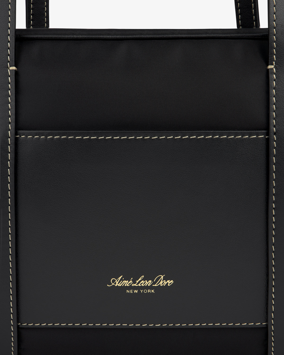 Close-up of a black Mini Duffle Shoulder Bag by Aimé Leon Dore with white stitching and gold logo on front pocket.