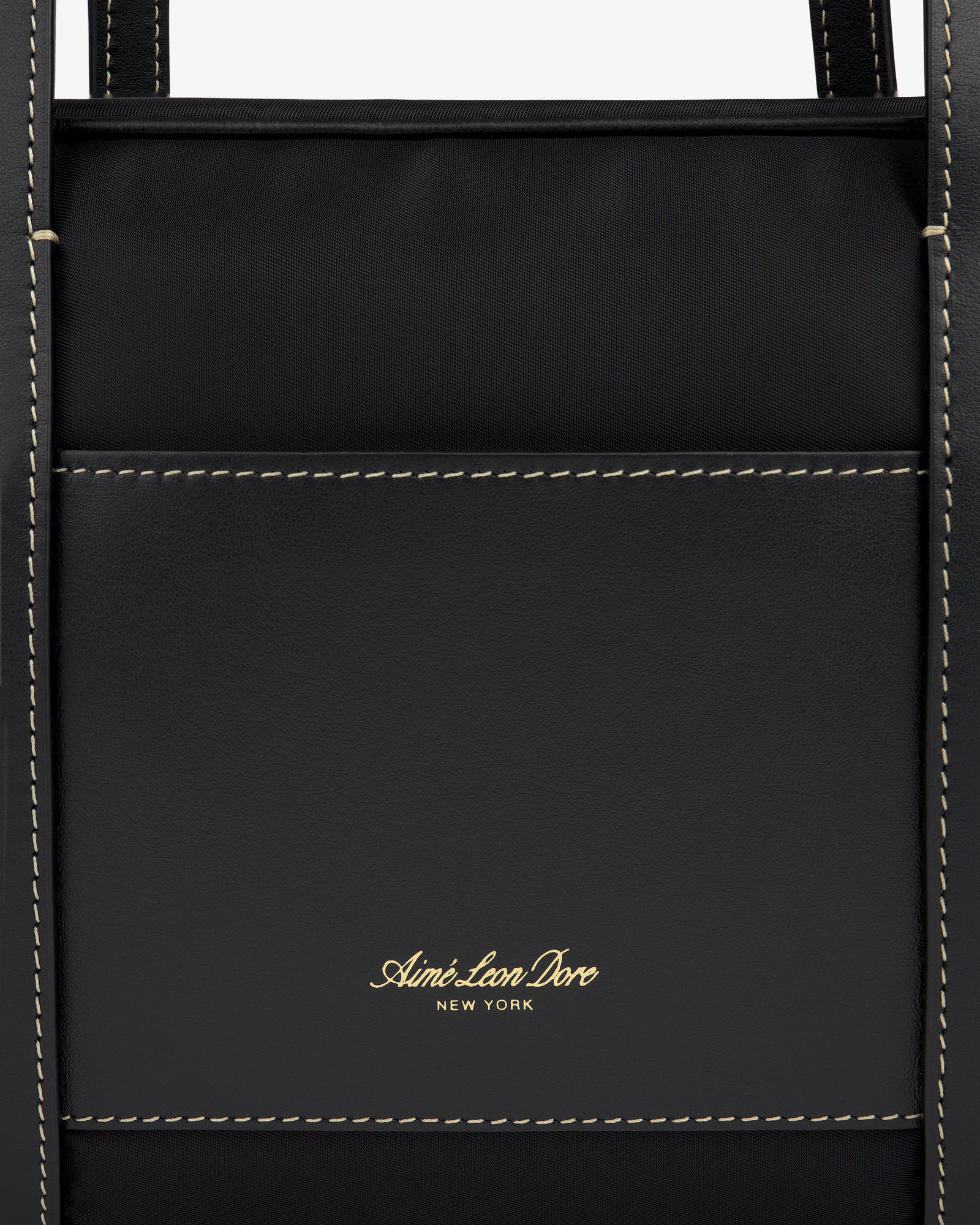 Close-up of a black Mini Duffle Shoulder Bag by Aimé Leon Dore with white stitching and gold logo on front pocket.
