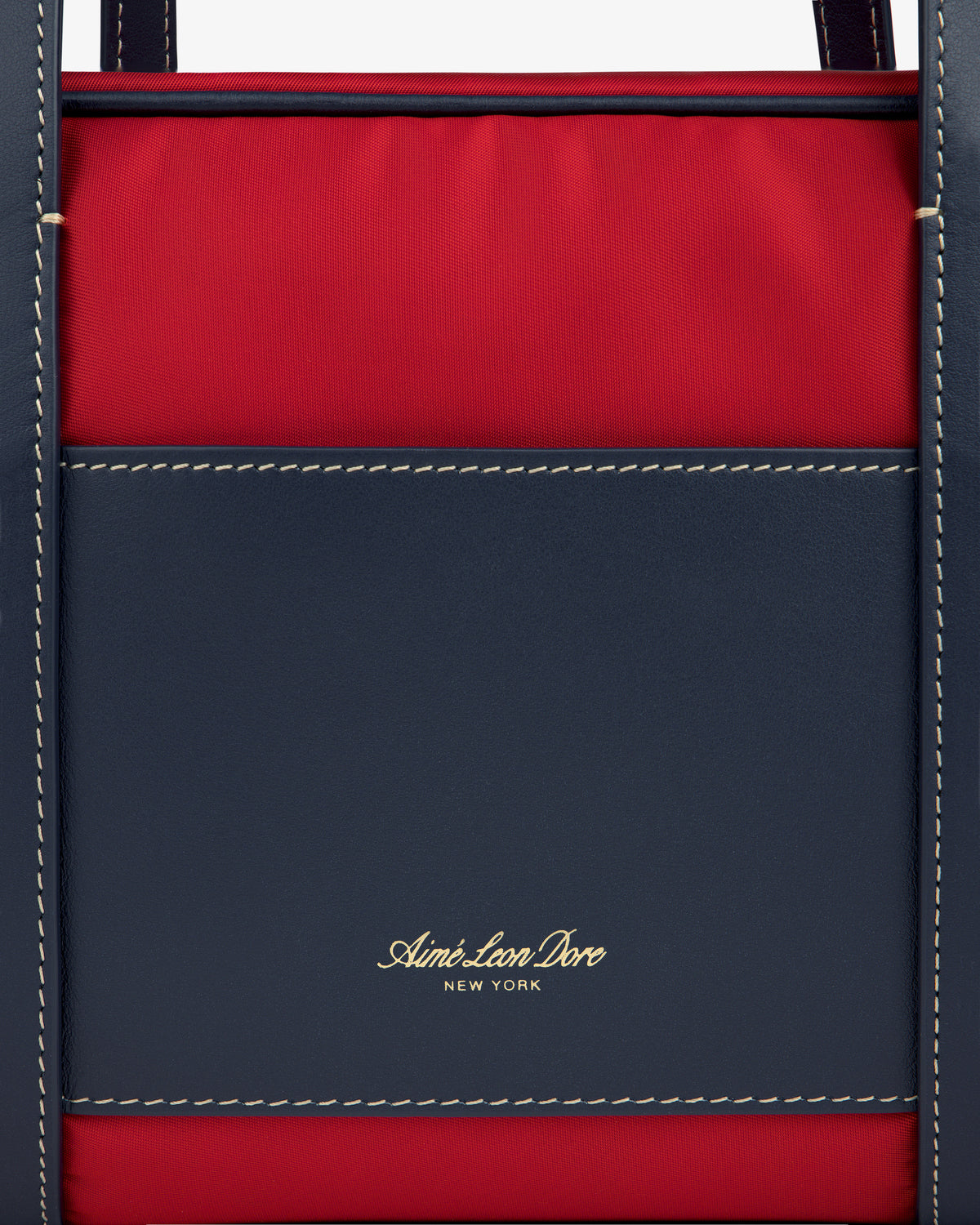 Close-up of a navy and red Mini Duffle Shoulder Bag with white stitching and gold Aimé Leon Dore New York text.
