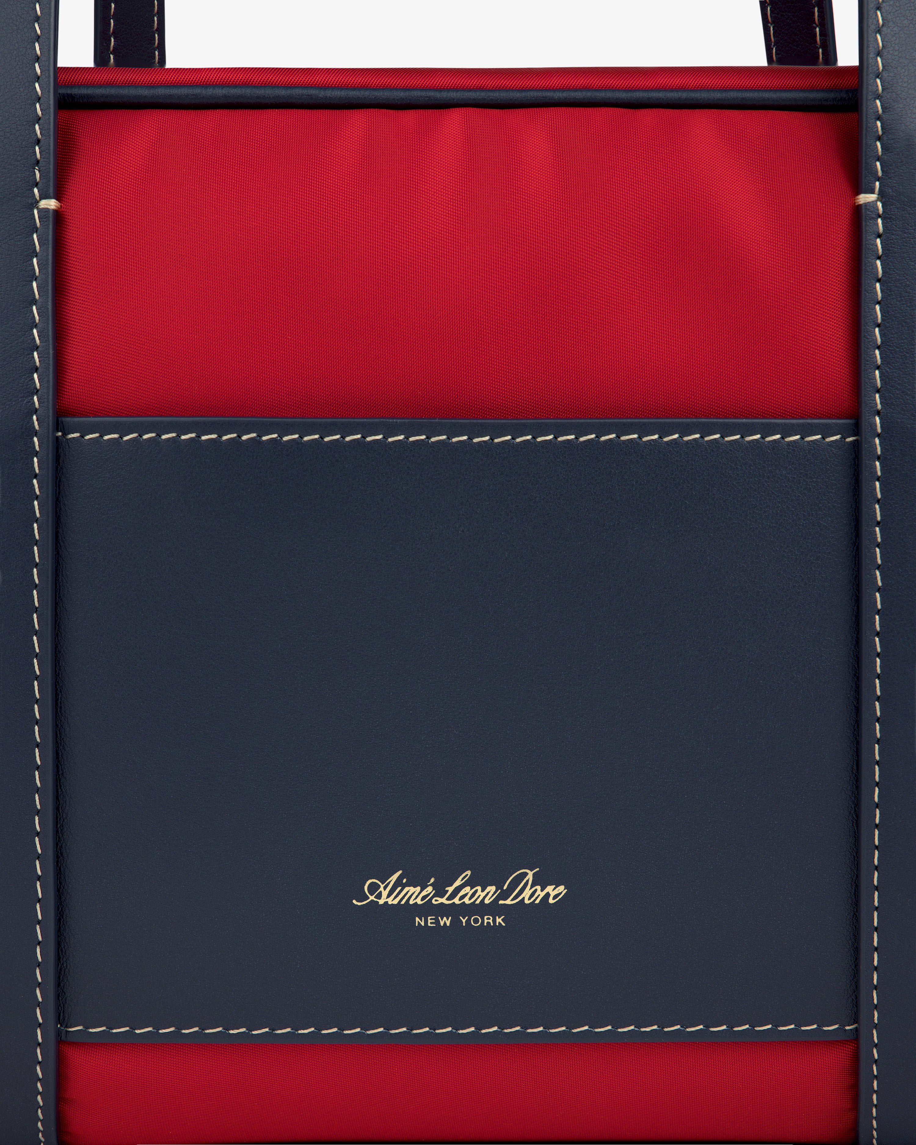Close-up of a navy and red Mini Duffle Shoulder Bag with white stitching and gold Aimé Leon Dore New York text.