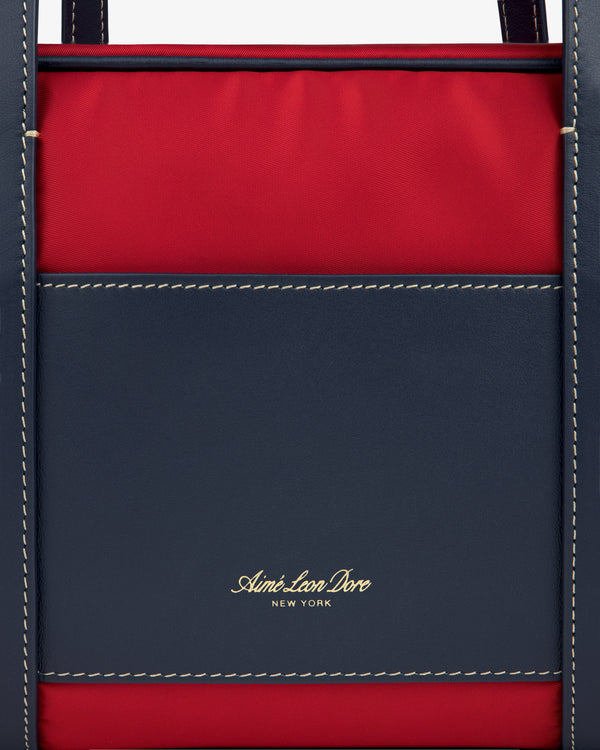 Close-up of a navy and red Mini Duffle Shoulder Bag with white stitching and gold Aimé Leon Dore New York text.