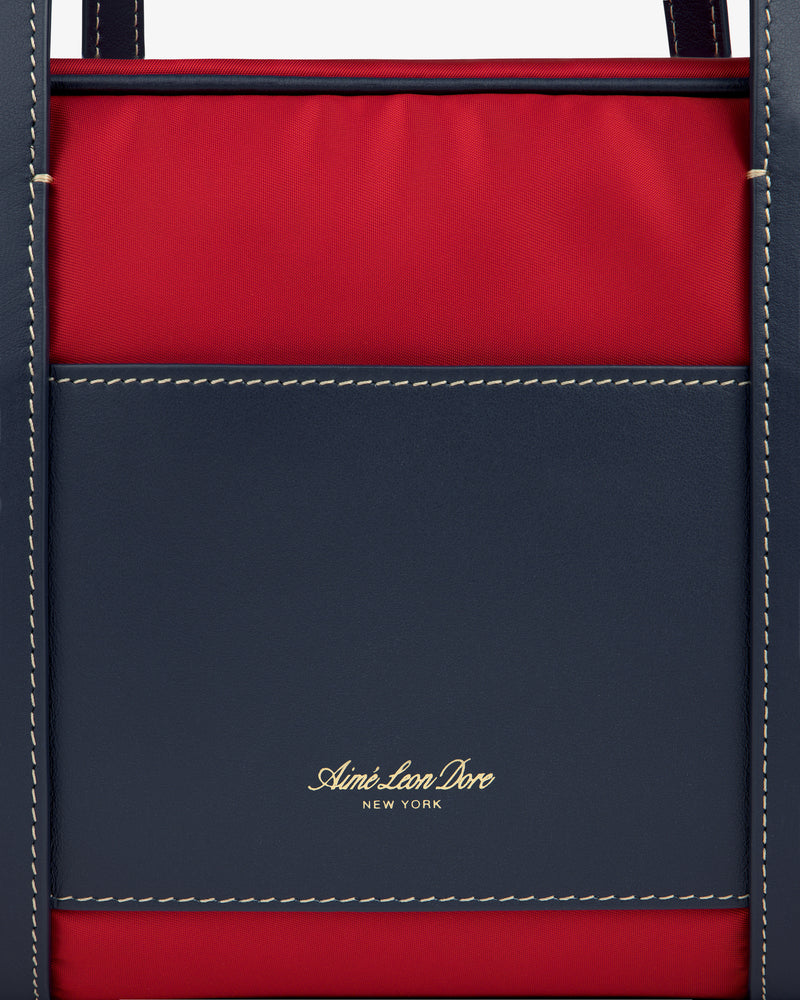 Close-up of a navy and red Mini Duffle Shoulder Bag with white stitching and gold Aimé Leon Dore New York text.
