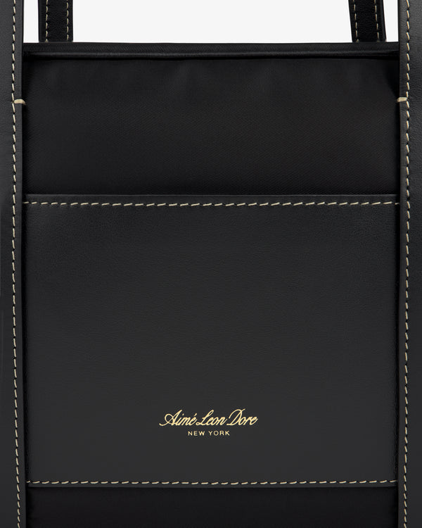 Close-up of a black Mini Duffle Shoulder Bag by Aimé Leon Dore with white stitching and gold logo on front pocket.