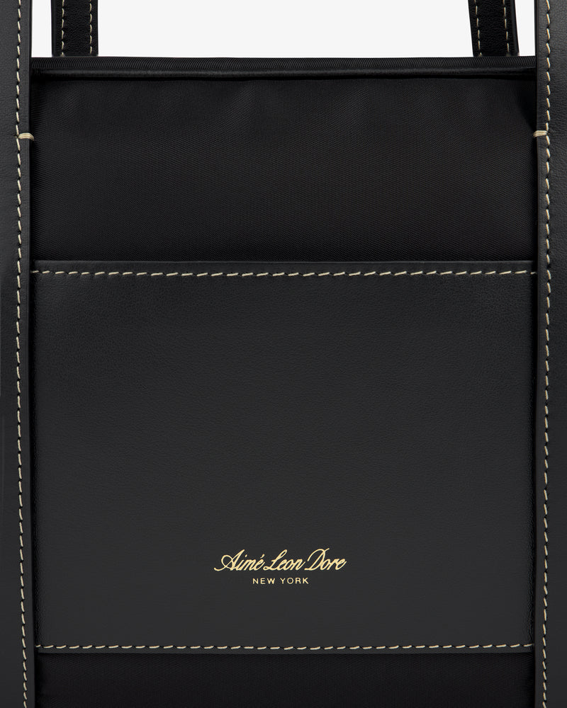 Close-up of a black Mini Duffle Shoulder Bag by Aimé Leon Dore with white stitching and gold logo on front pocket.