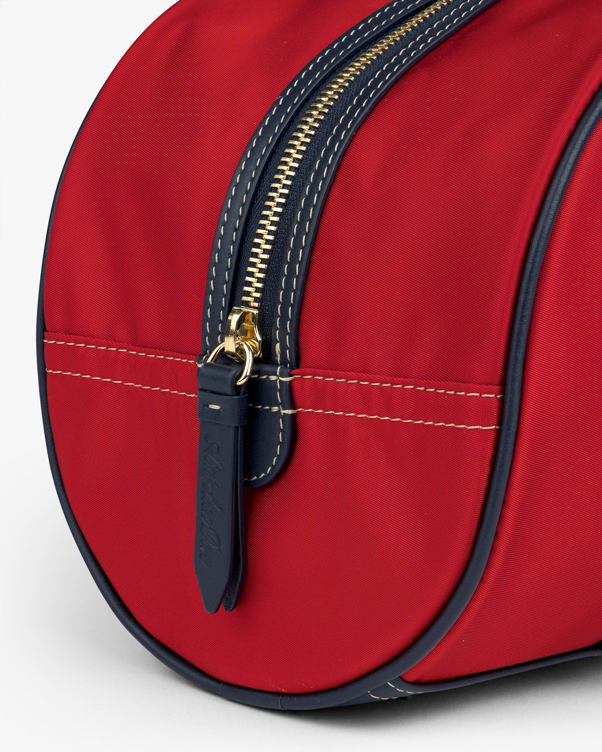 Close-up of the Mini Duffle Shoulder Bag in red with a gold zipper, navy trim, and leather zipper pull.