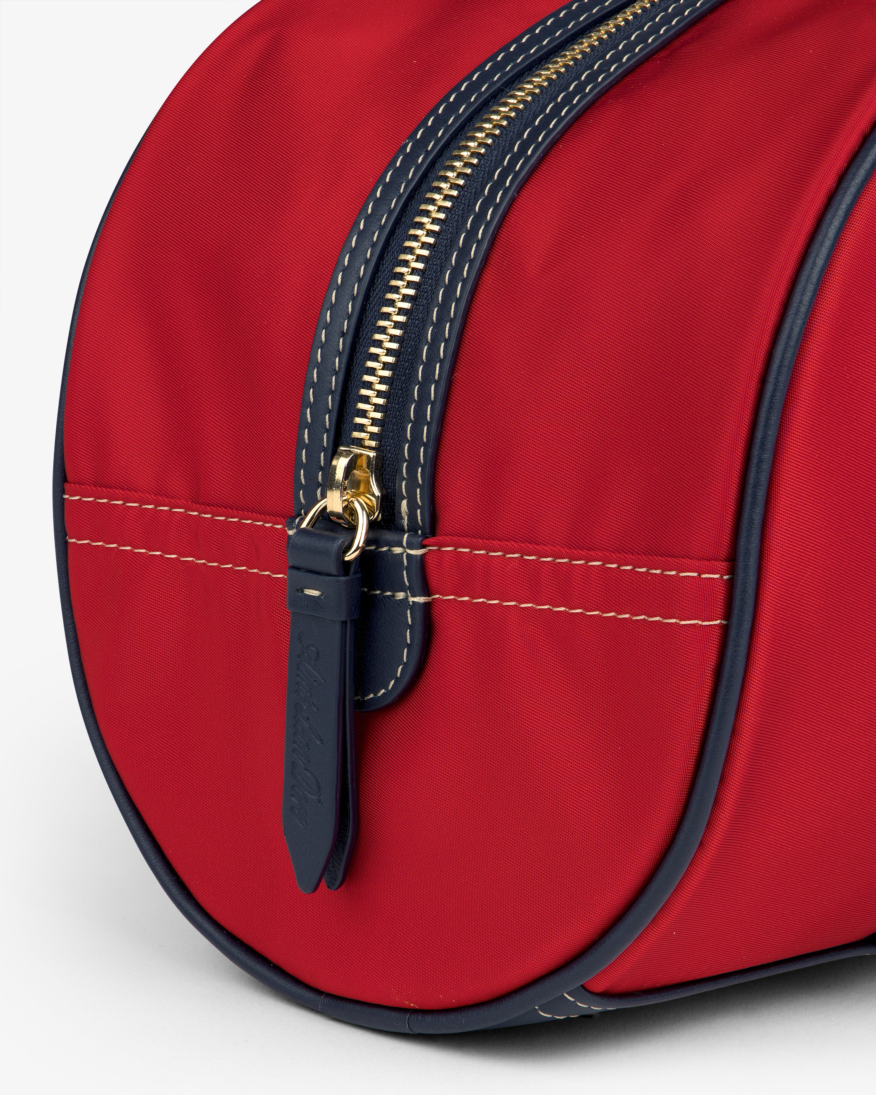 Close-up of the Mini Duffle Shoulder Bag in red with a gold zipper, navy trim, and leather zipper pull.