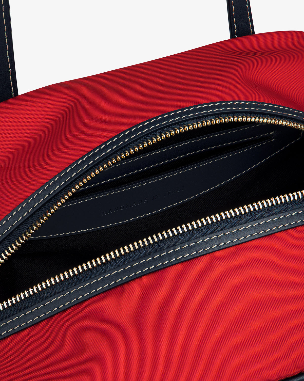 Close-up of the Mini Duffle Shoulder Bag in red with a partially open zipper, dark interior, and white stitching.