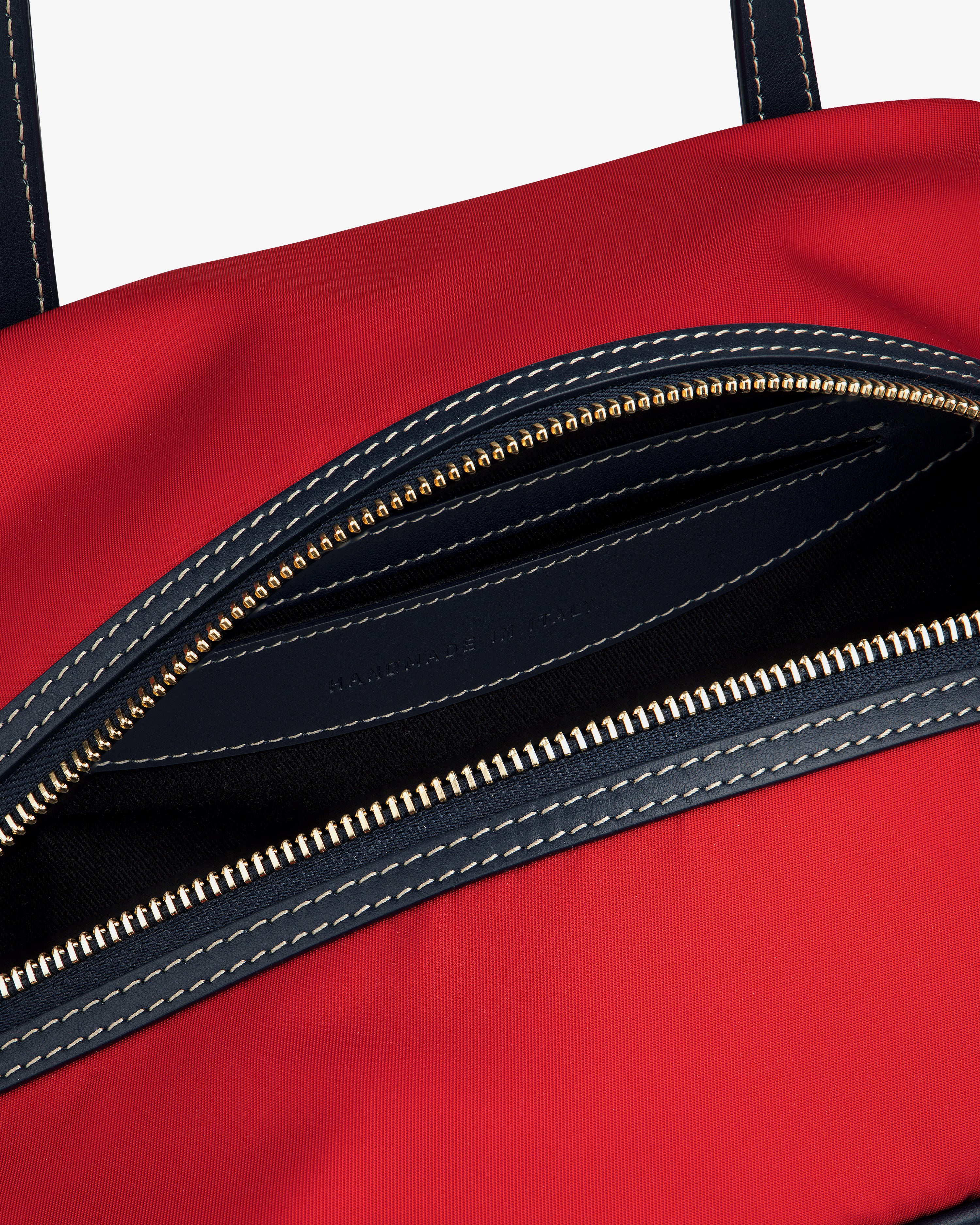 Close-up of the Mini Duffle Shoulder Bag in red with a partially open zipper, dark interior, and white stitching.