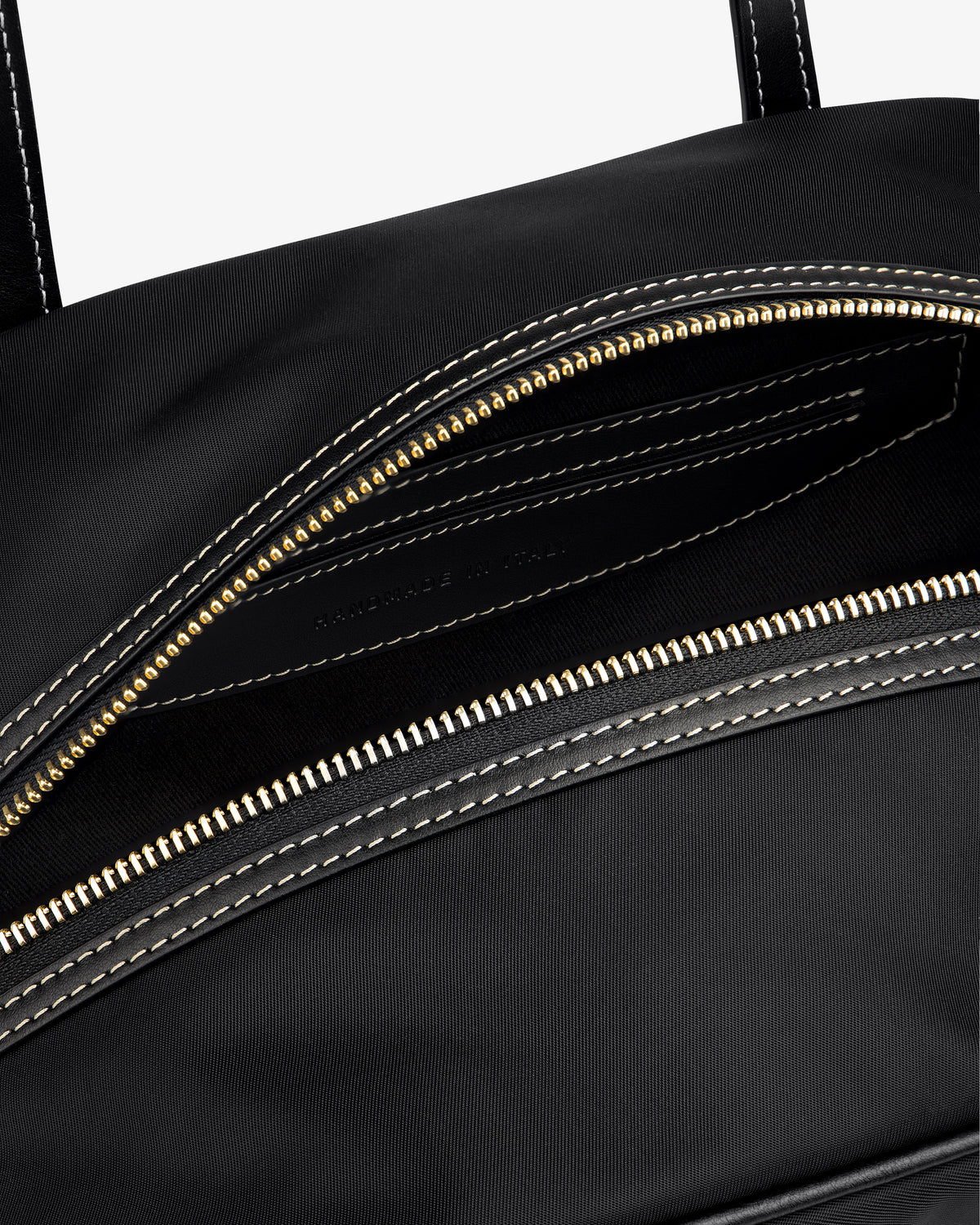 Close-up of the Mini Duffle Shoulder Bag in black with a gold zipper and white stitching around the opening.