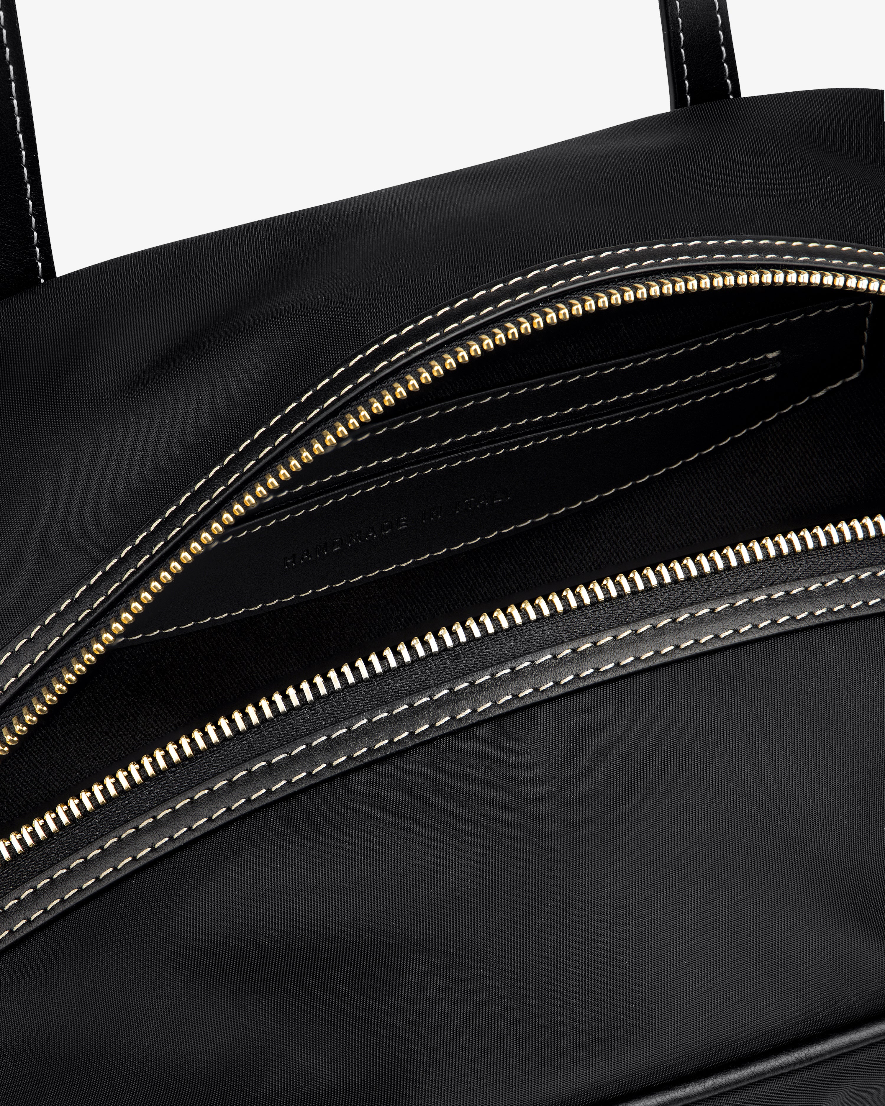 Close-up of the Mini Duffle Shoulder Bag in black with a gold zipper and white stitching around the opening.