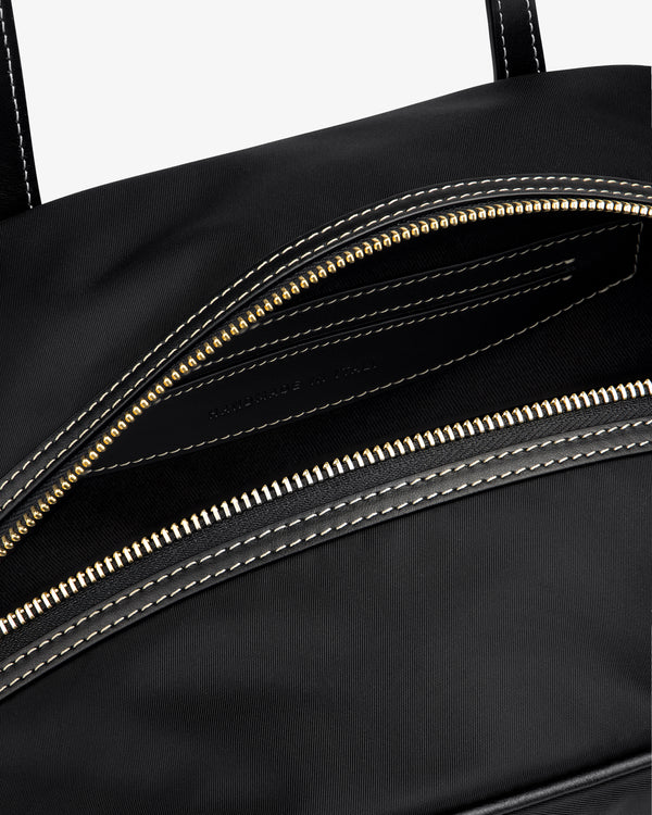 Close-up of the Mini Duffle Shoulder Bag in black with a gold zipper and white stitching around the opening.