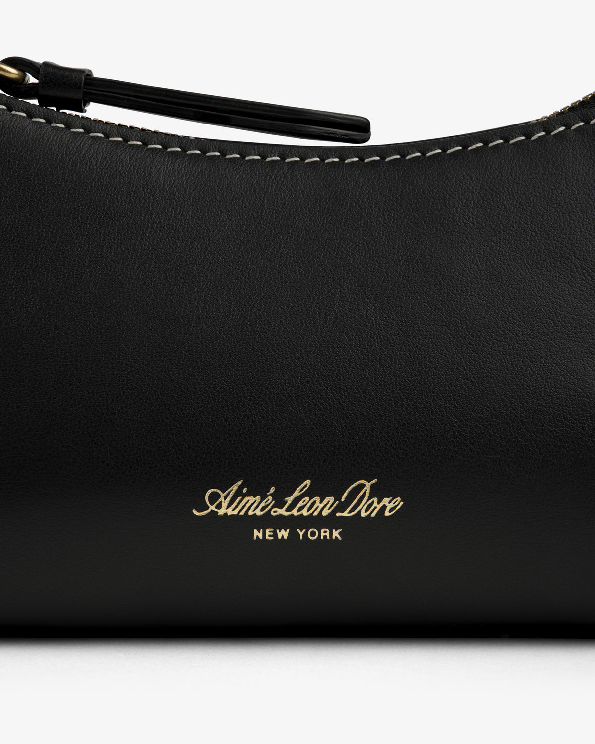 Close-up of the Convertible Leather Belt Bag with gold Aimé Leon Dore NEW YORK embossing and visible white stitching.