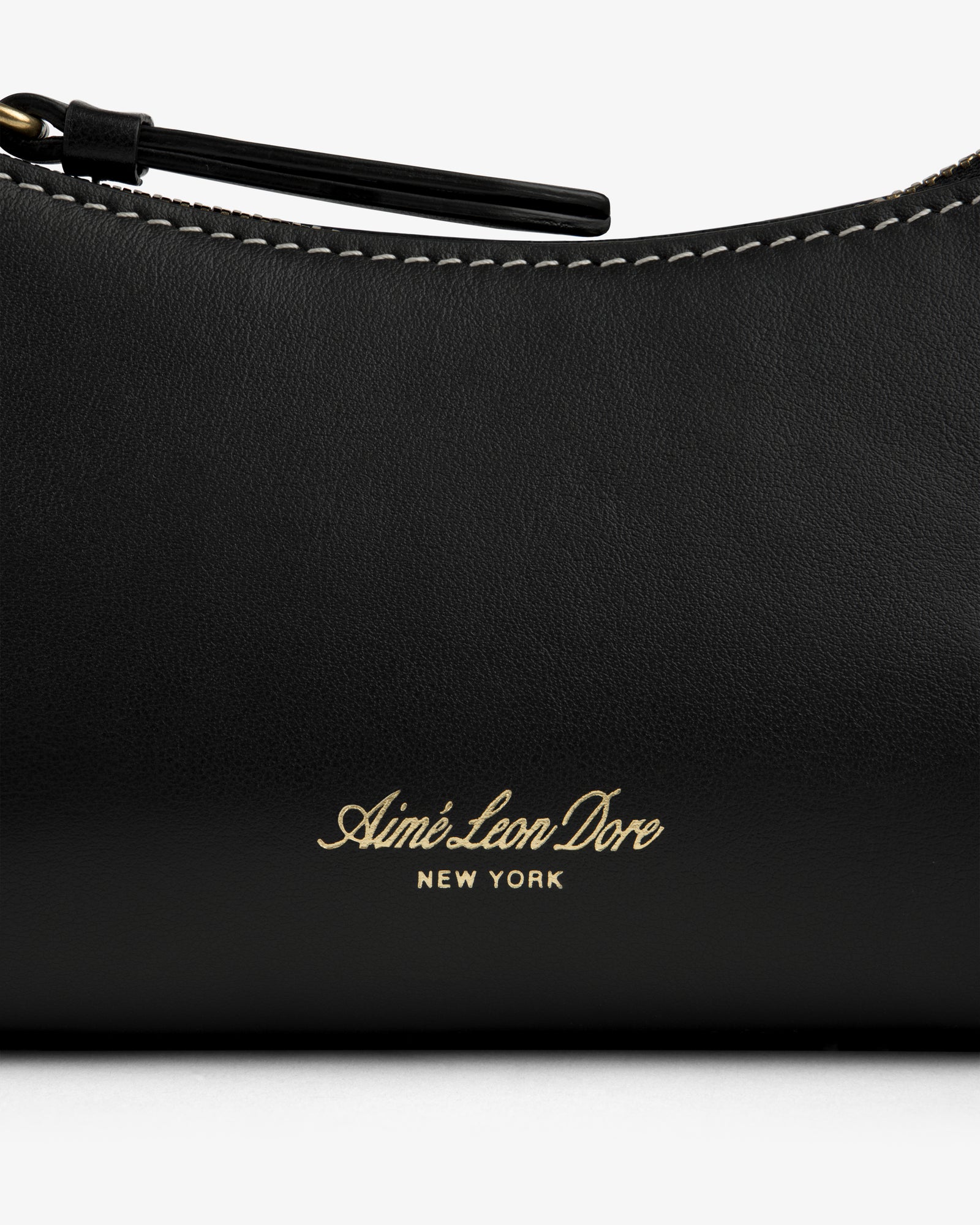 Close-up of the Convertible Leather Belt Bag with gold Aimé Leon Dore NEW YORK embossing and visible white stitching.