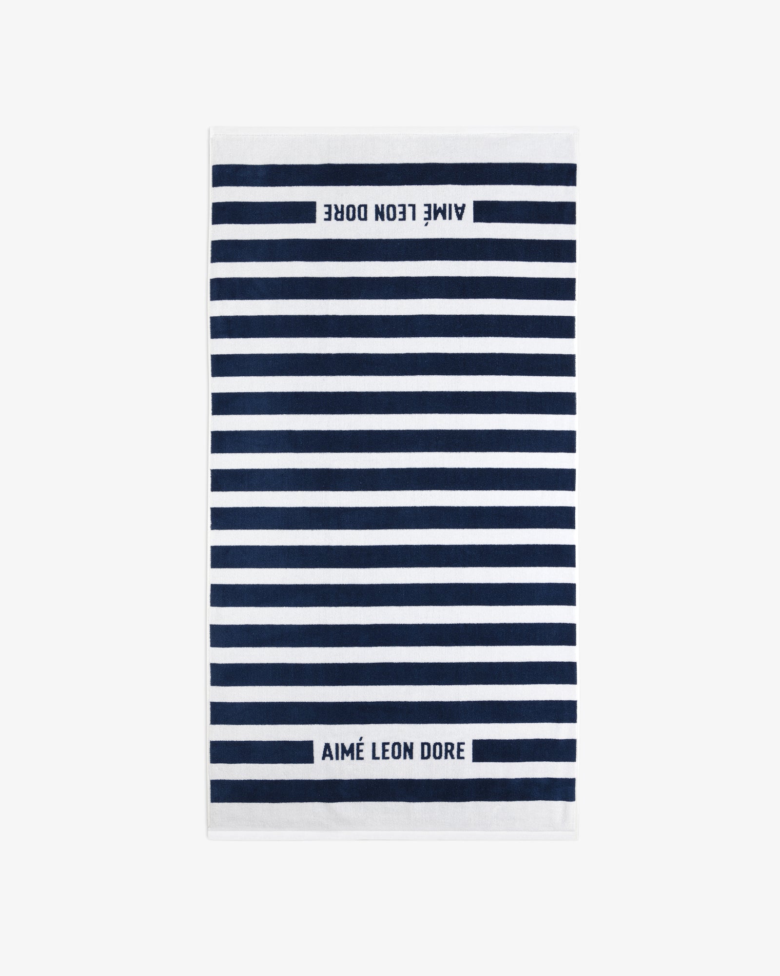 The Striped Beach Towel is white with navy blue horizontal stripes and AIMÉ LEON DORE text on both ends.