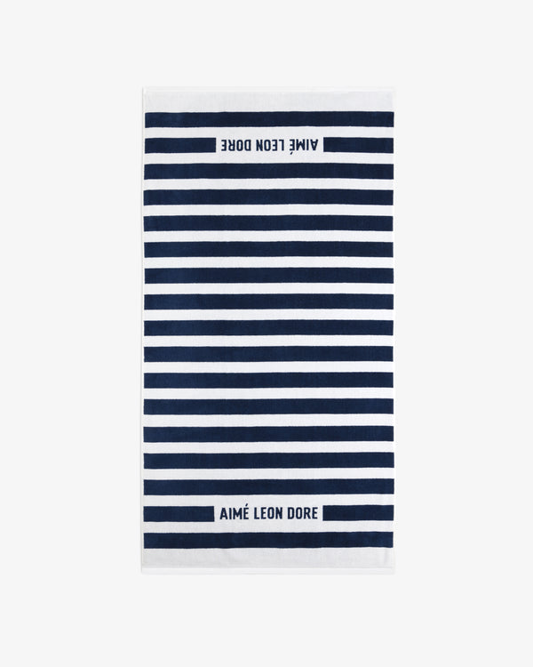 The Striped Beach Towel is white with navy blue horizontal stripes and AIMÉ LEON DORE text on both ends.