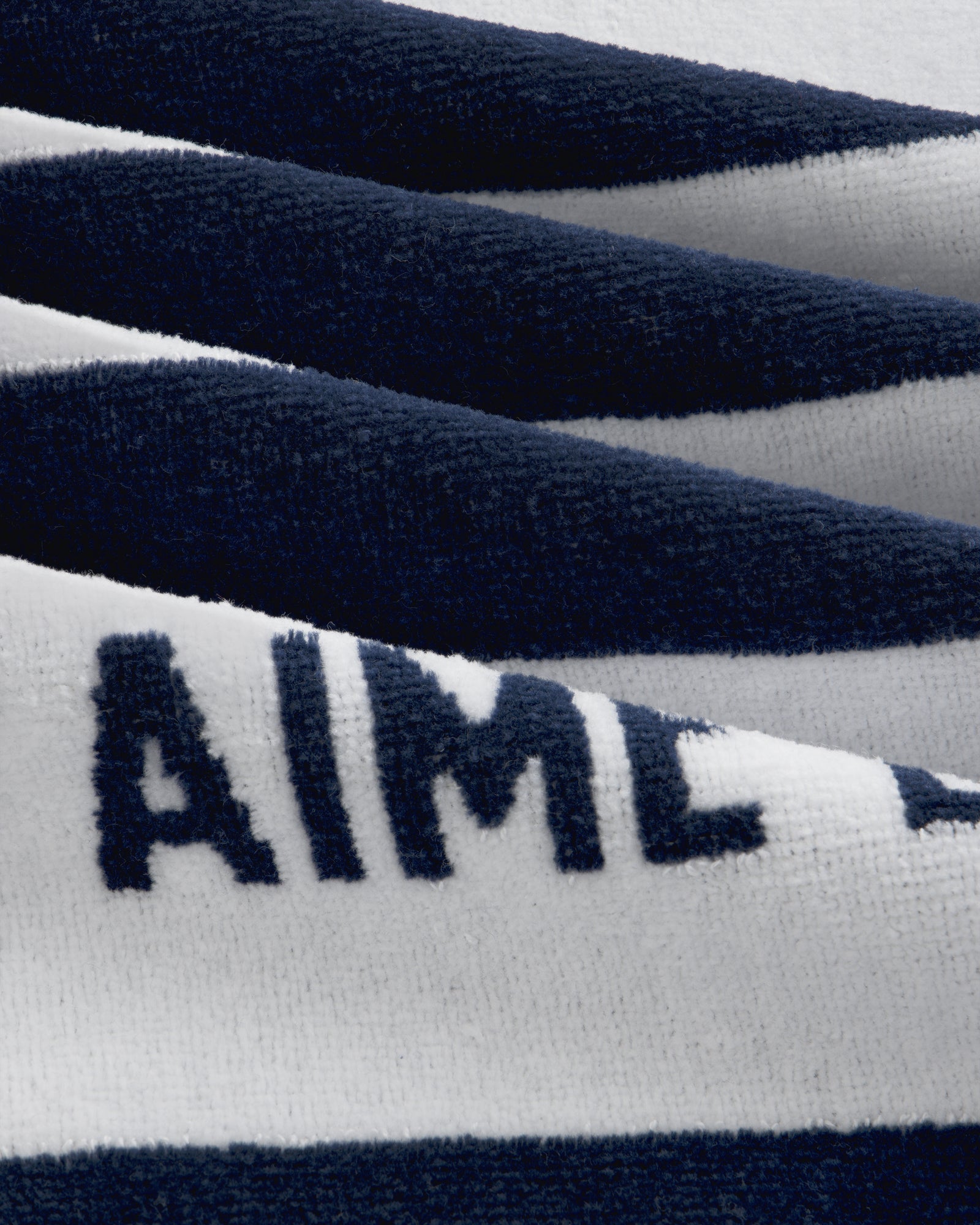 Close-up of the Striped Beach Towel, showing its soft navy and white stripes with “AIME” partly visible on the fabric.