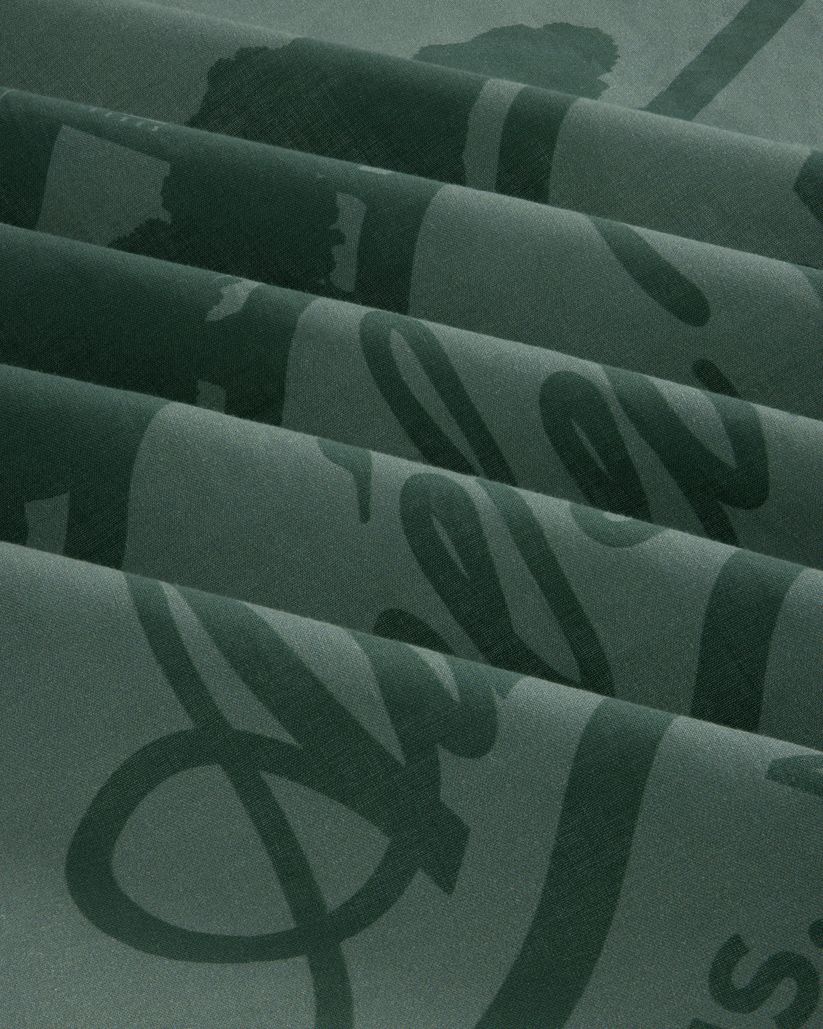 Sun Faded Unisphere Bandana in dark green with a glossy script design, folded to form diagonal ridges and shadows.