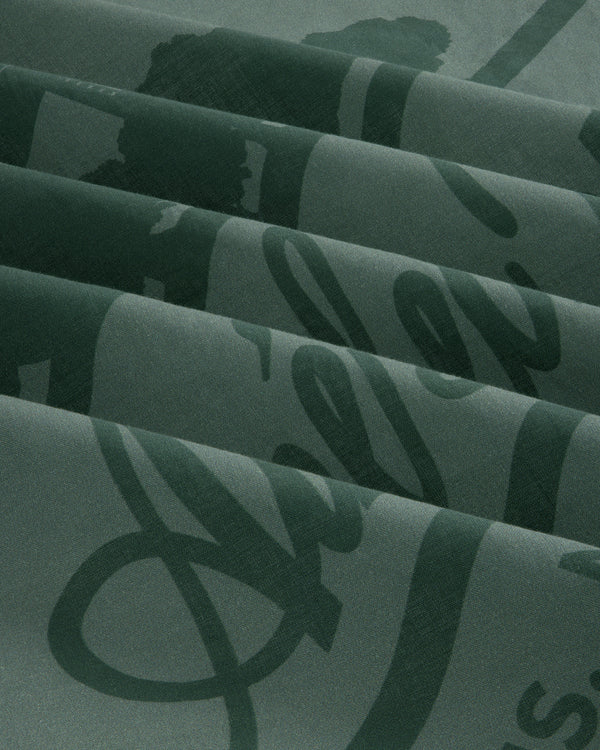 Sun Faded Unisphere Bandana in dark green with a glossy script design, folded to form diagonal ridges and shadows.