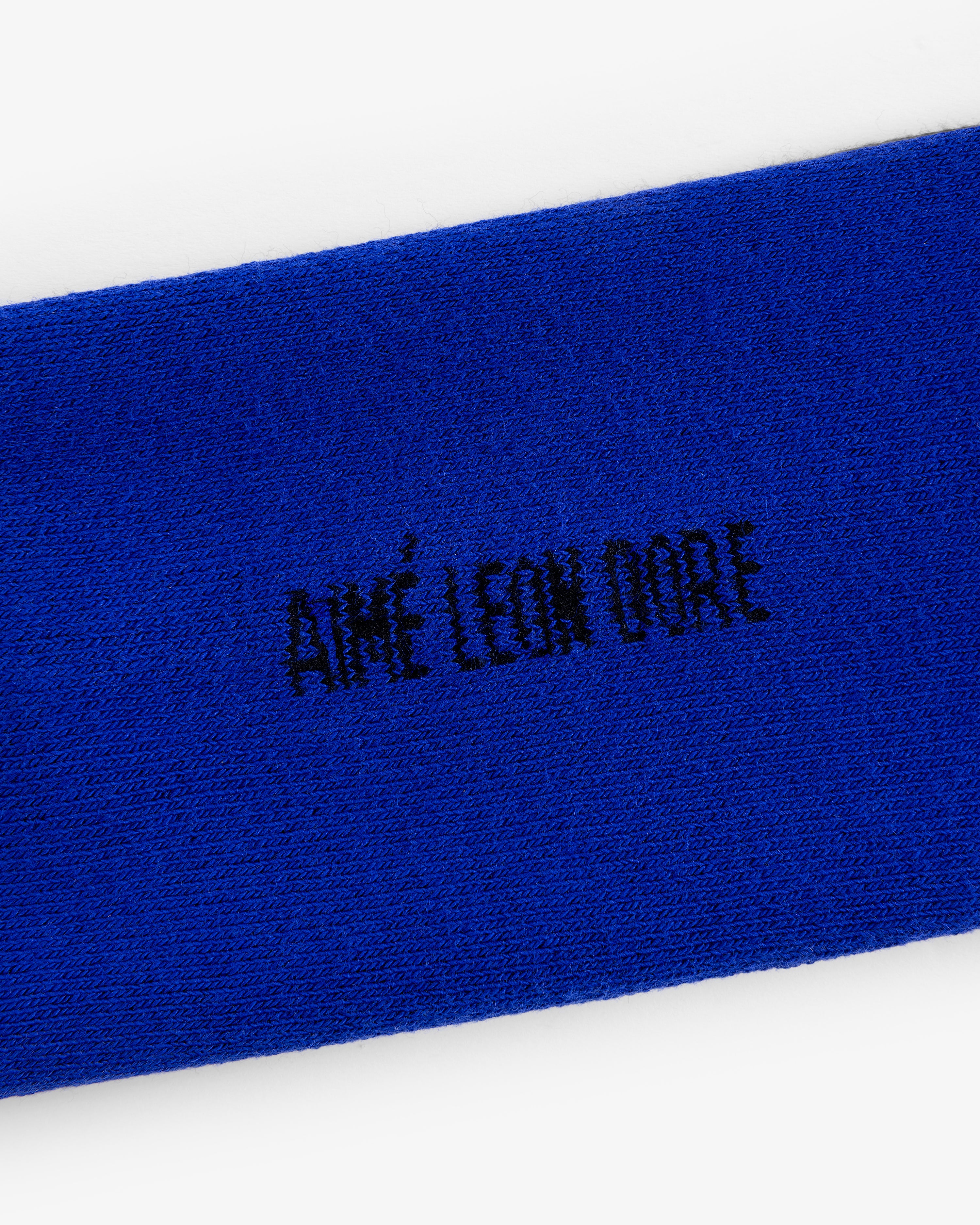Close-up of blue fabric with black AIMÉ LEON DORE embroidery from the Crew Sock 3-Pack.