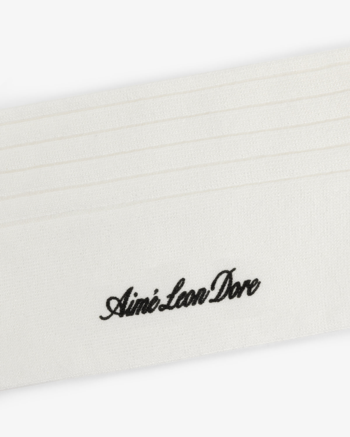 A white Dress Sock with black cursive Aimé Leon Dore embroidery and several stitched horizontal lines.