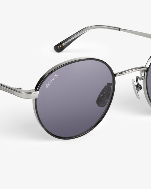 Close-up of Giórgios Sunglasses: silver round frames, dark purple lenses, and Saint Laurent Paris logo on the lens.