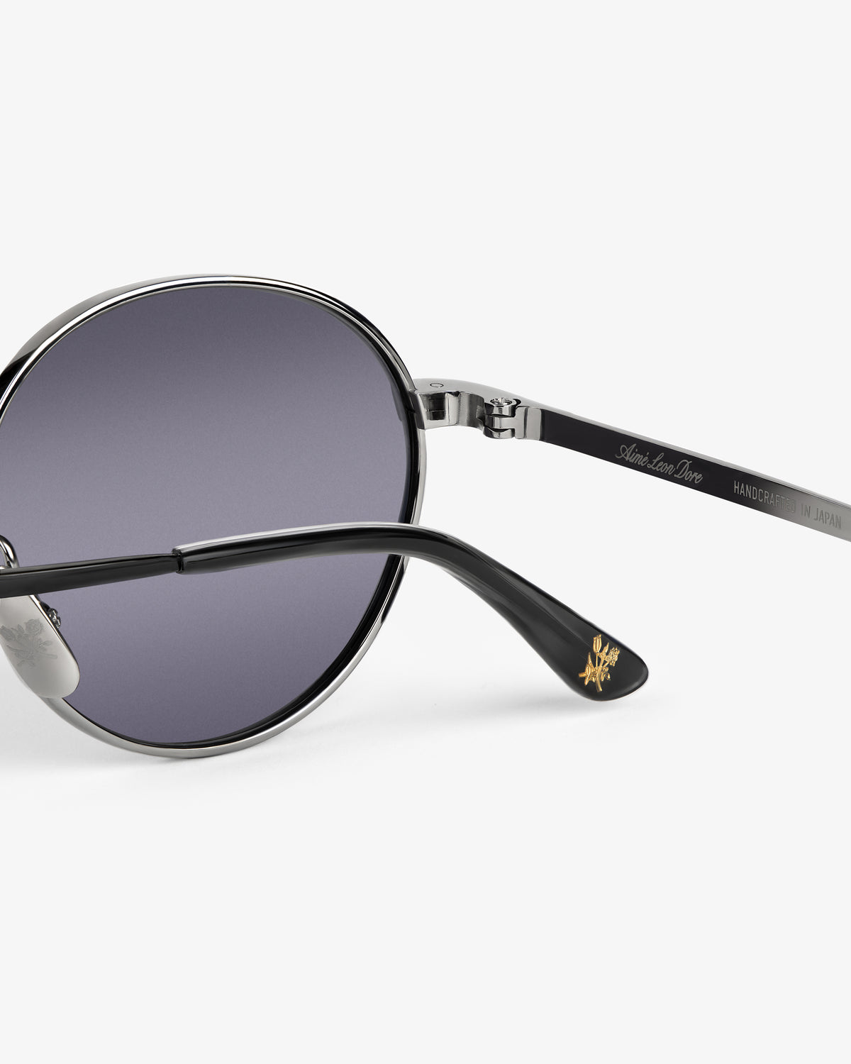 Close-up of Giórgios Sunglasses with dark lenses, silver frame, and black temple featuring gold logo detail on the tip.