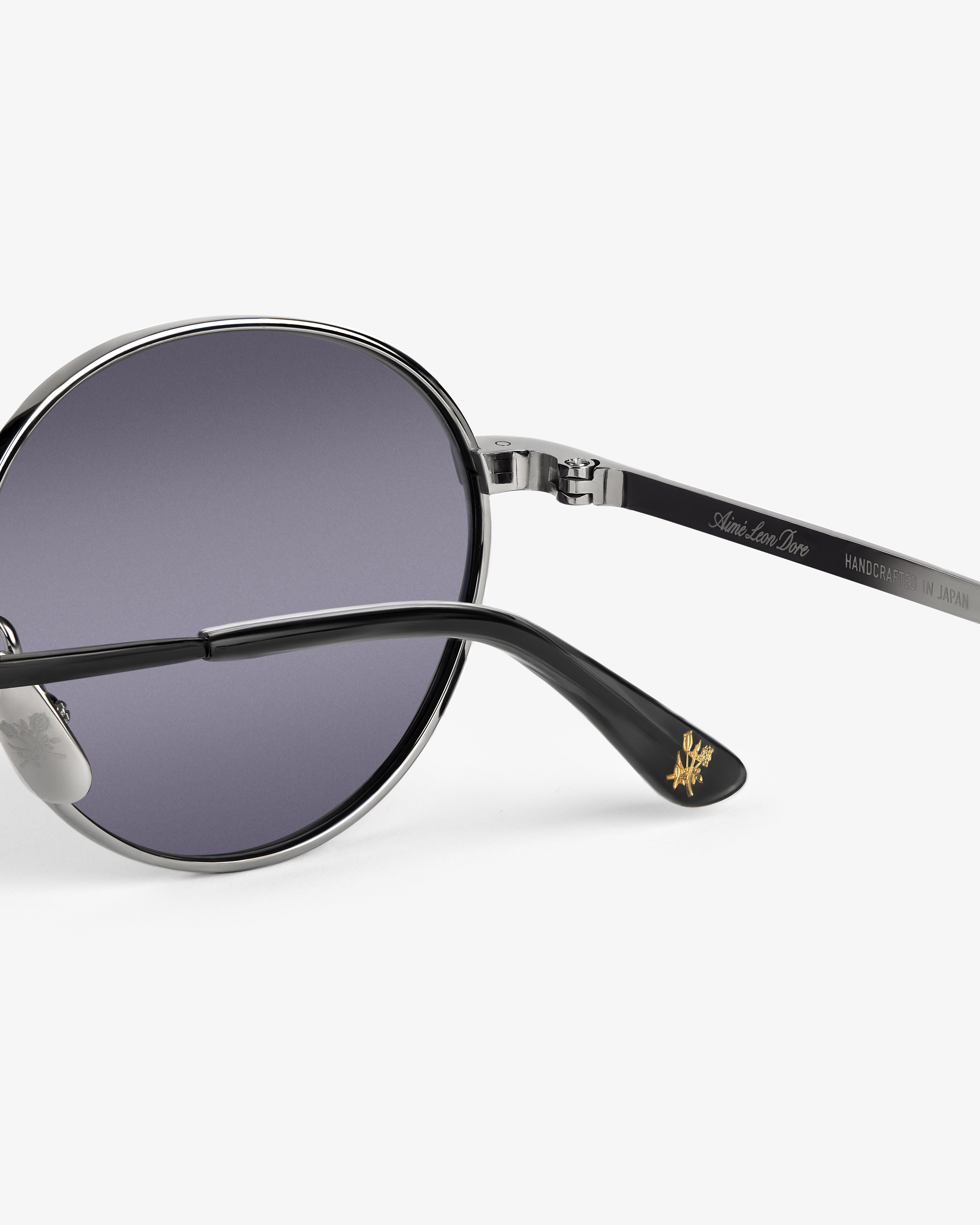 Close-up of Giórgios Sunglasses with dark lenses, silver frame, and black temple featuring gold logo detail on the tip.