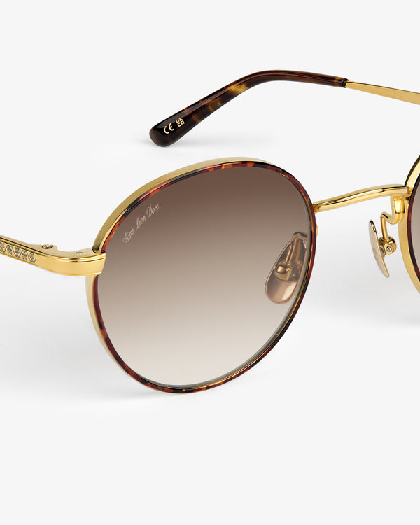 Close-up of Giórgios Sunglasses—gold and tortoiseshell rounds with brown gradient lenses on white background.