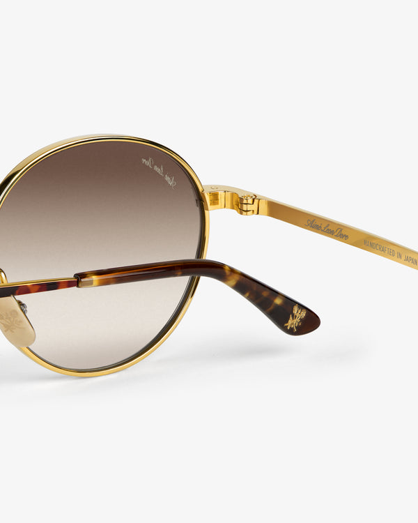 Close-up of Giórgios Sunglasses: gold frame, brown gradient lenses, and tortoiseshell arms with intricate detailing.