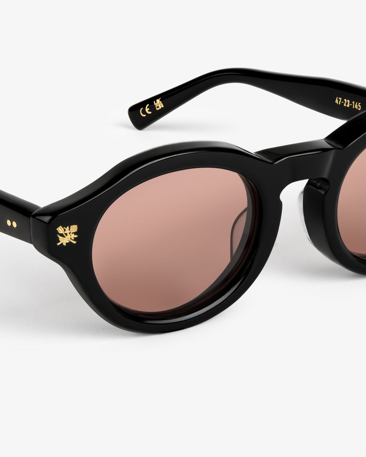 Onásis Sunglasses: black round frames with brown lenses, gold temple and hinge detailing on a white background.