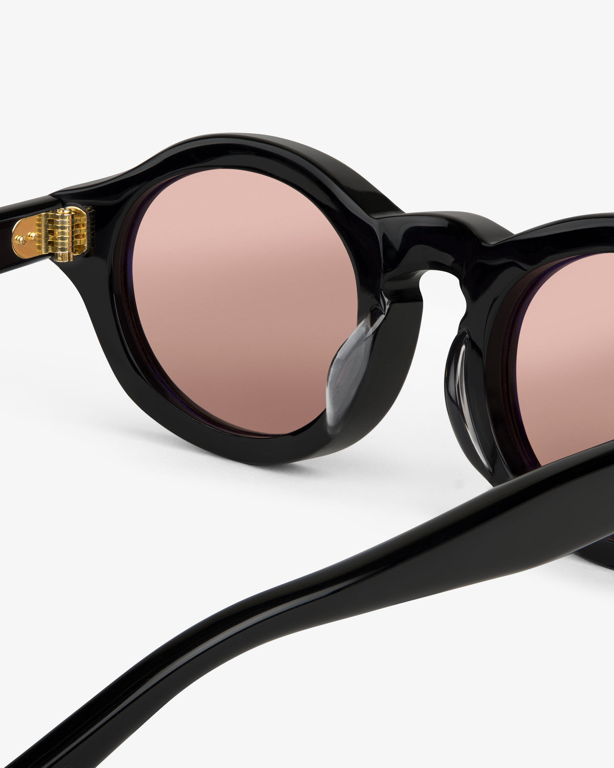 Close-up of Onásis Sunglasses—black round frames with pink tinted lenses on a plain white background.