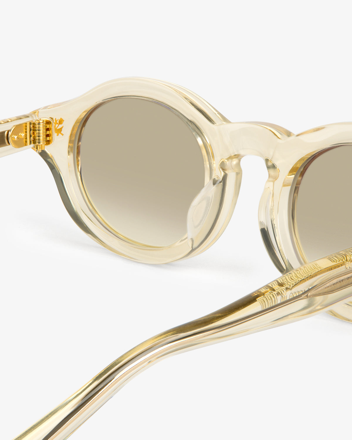 Onásis Sunglasses: round, clear frames with gold accents and light brown tinted lenses on a white background.