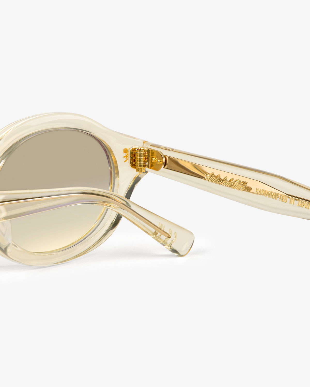 Close-up of Onásis Sunglasses: translucent beige frames, gold accents, and "Handcrafted in Japan" on the arm.