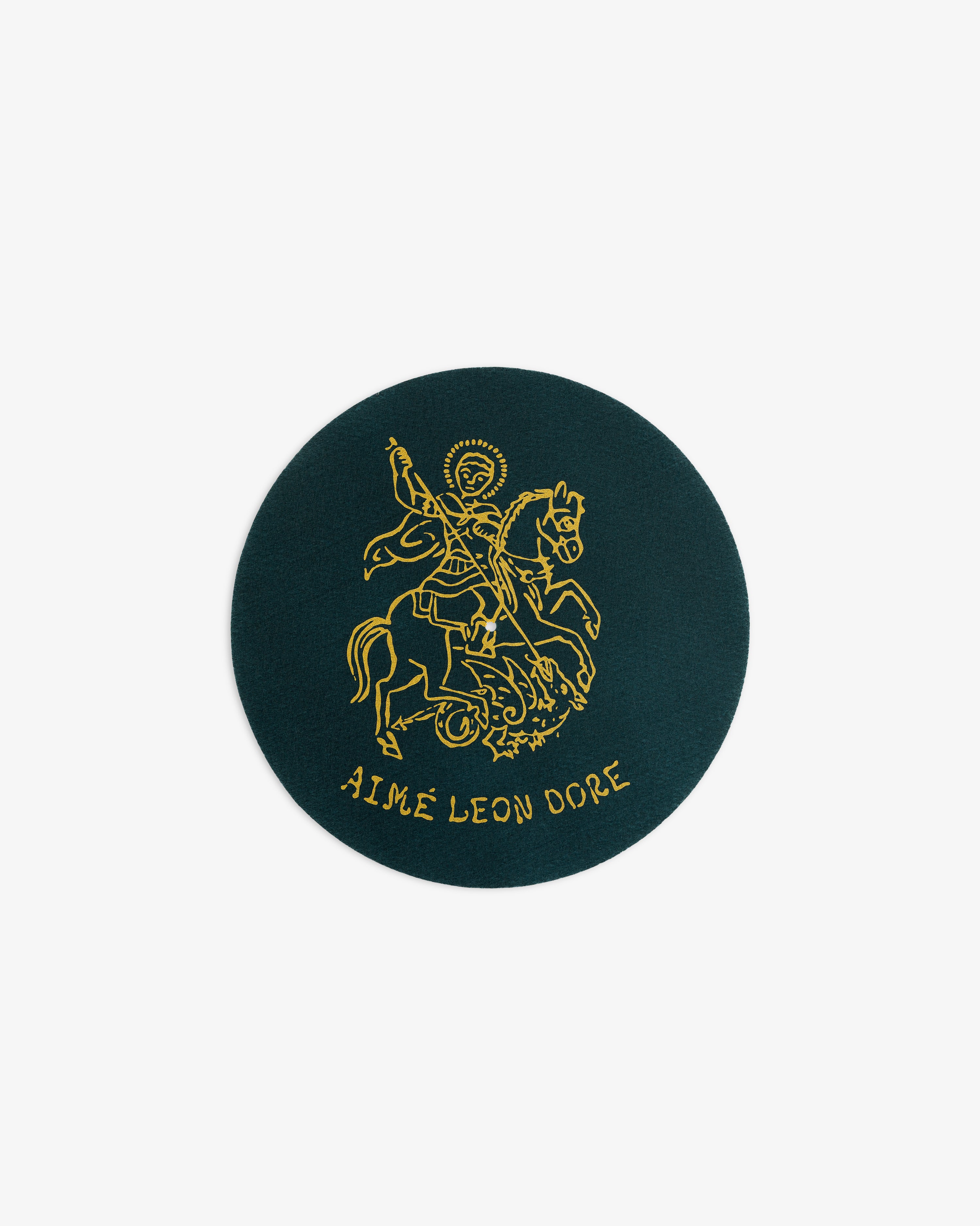 A round dark green patch from Graphic Slip Mats with a gold line drawing of a rider and AIMÉ LEON DORE below.