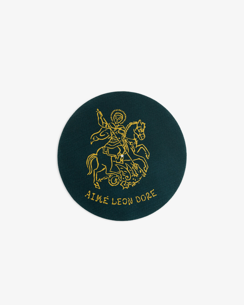 A round dark green patch from Graphic Slip Mats with a gold line drawing of a rider and AIMÉ LEON DORE below.