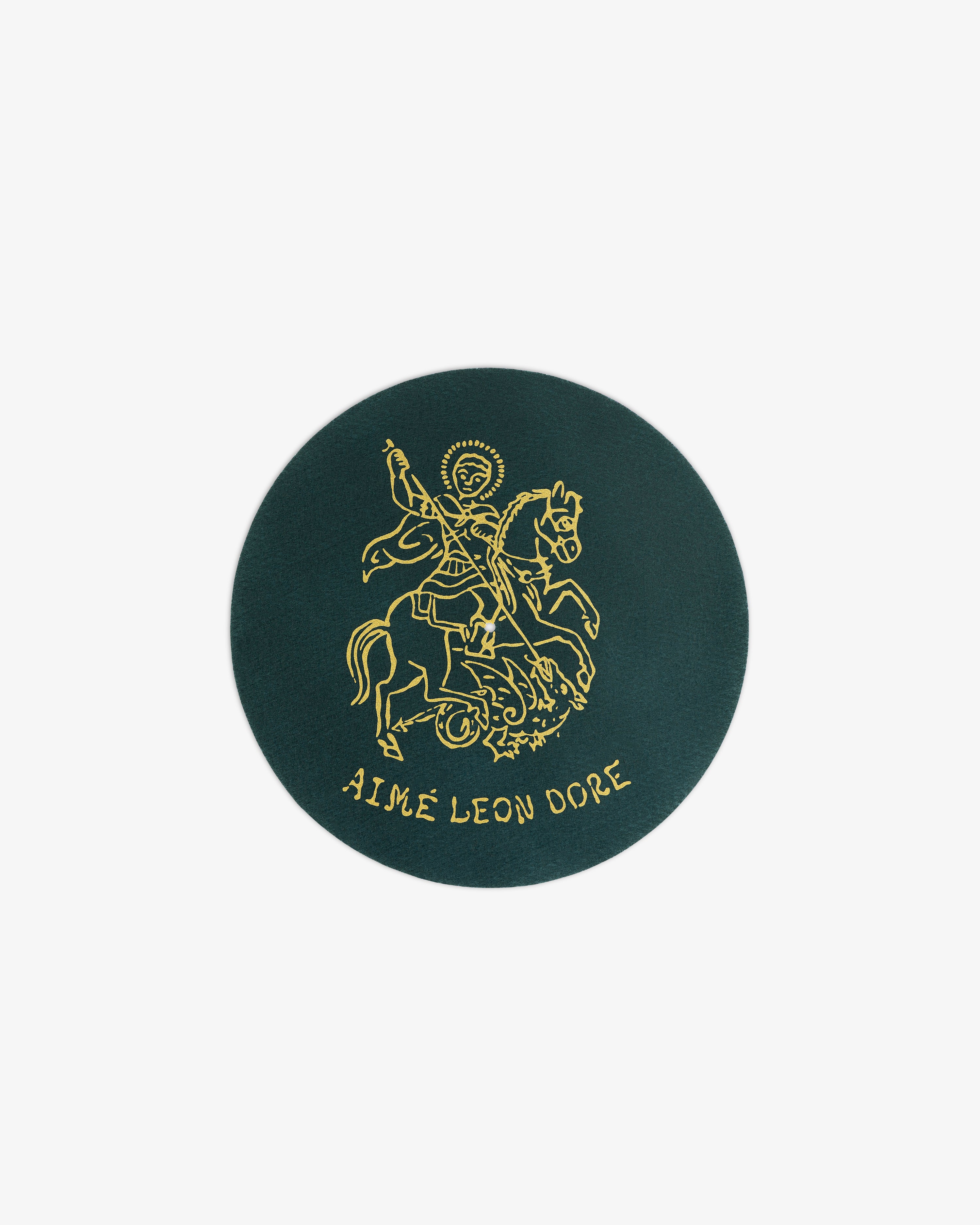 Dark green circular Graphic Slip Mats with a gold line drawing of a saint on horseback and AIMÉ LEON DORE below.