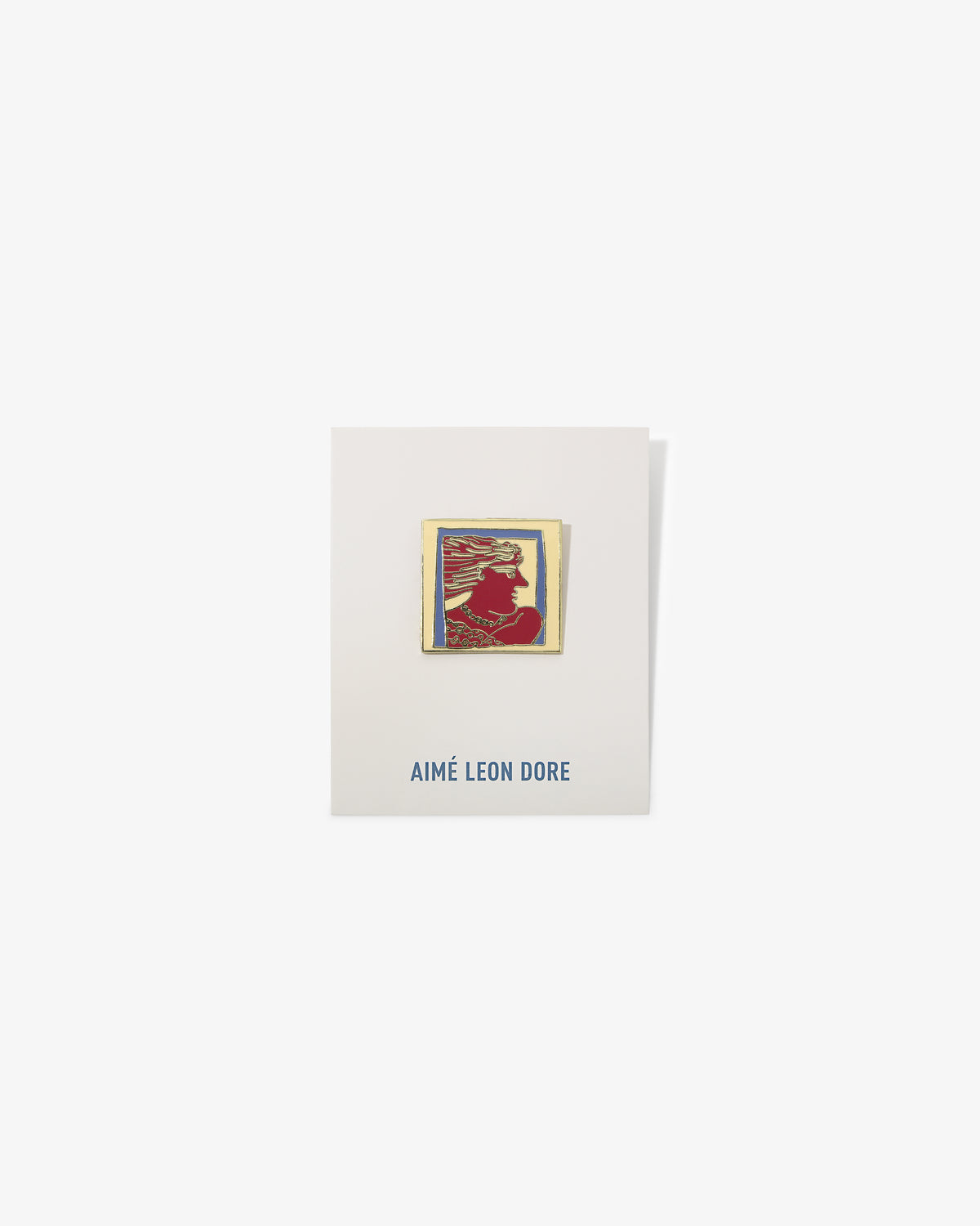 The Graphic Pin is a rectangular enamel pin with a red silhouette on an AIMÉ LEON DORE card in blue text.