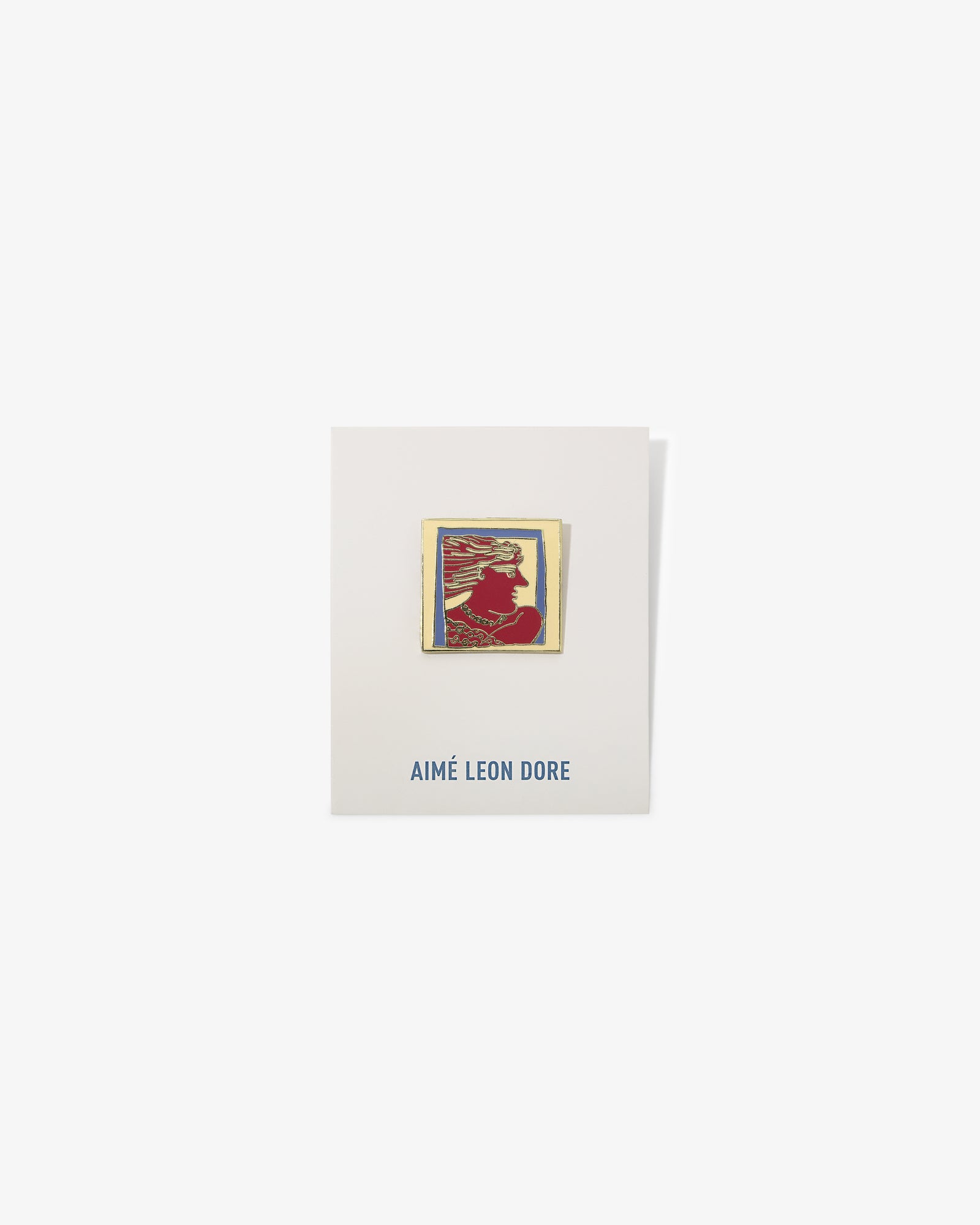The Graphic Pin is a rectangular enamel pin with a red silhouette on an AIMÉ LEON DORE card in blue text.