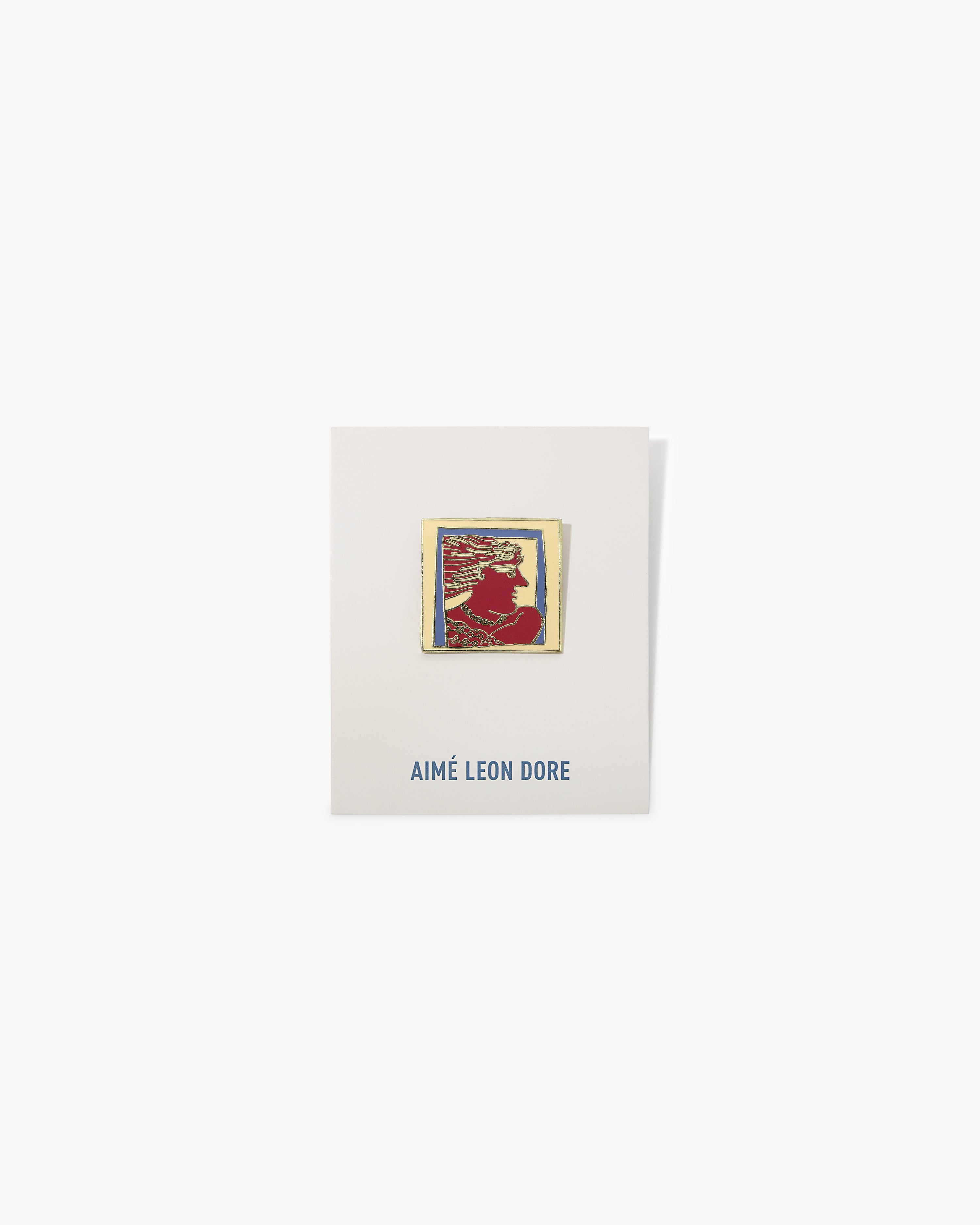 The Graphic Pin is a rectangular enamel pin with a red silhouette on an AIMÉ LEON DORE card in blue text.