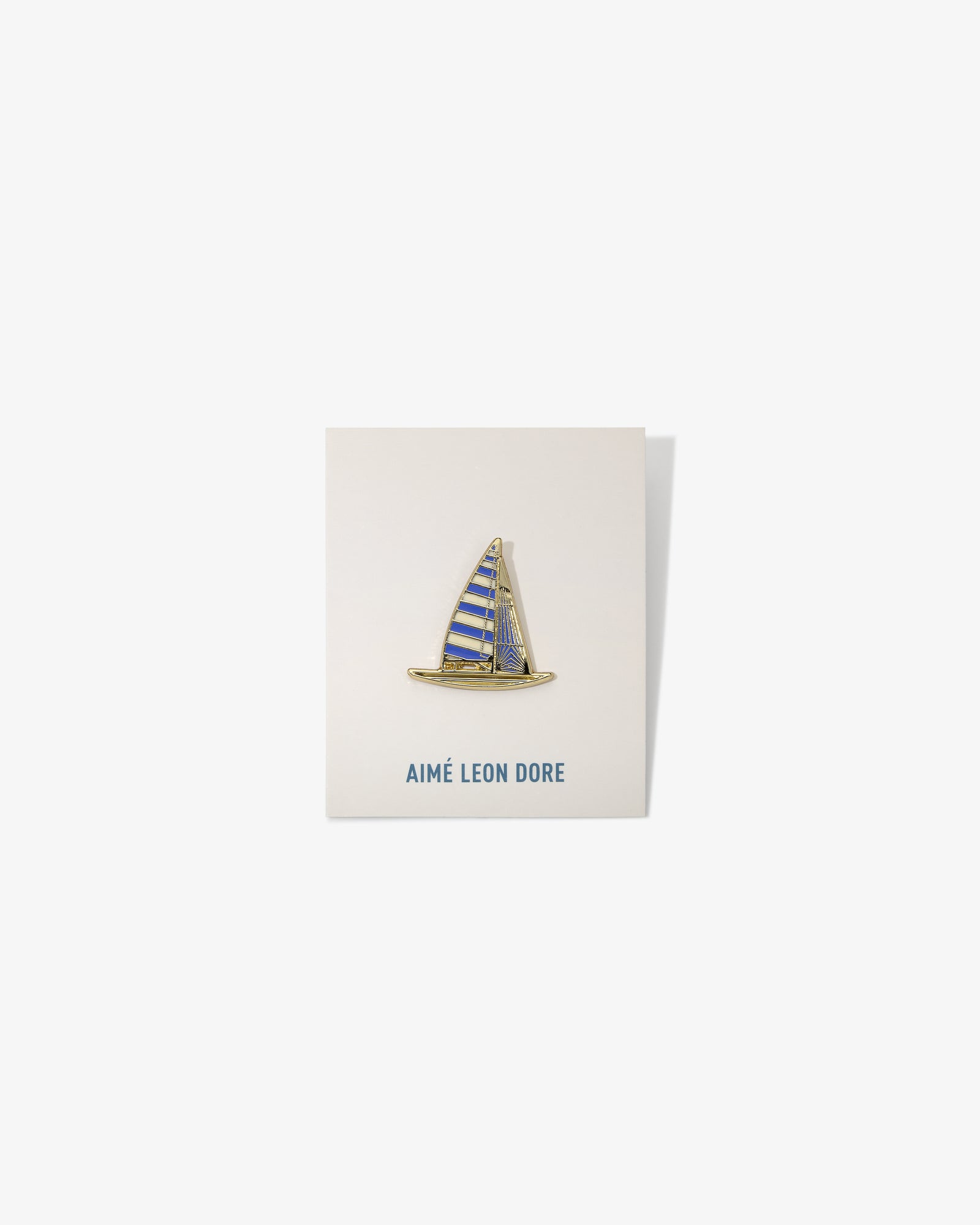 Graphic Pin featuring a sailboat with blue and yellow stripes, mounted on an AIMÉ LEON DORE card.