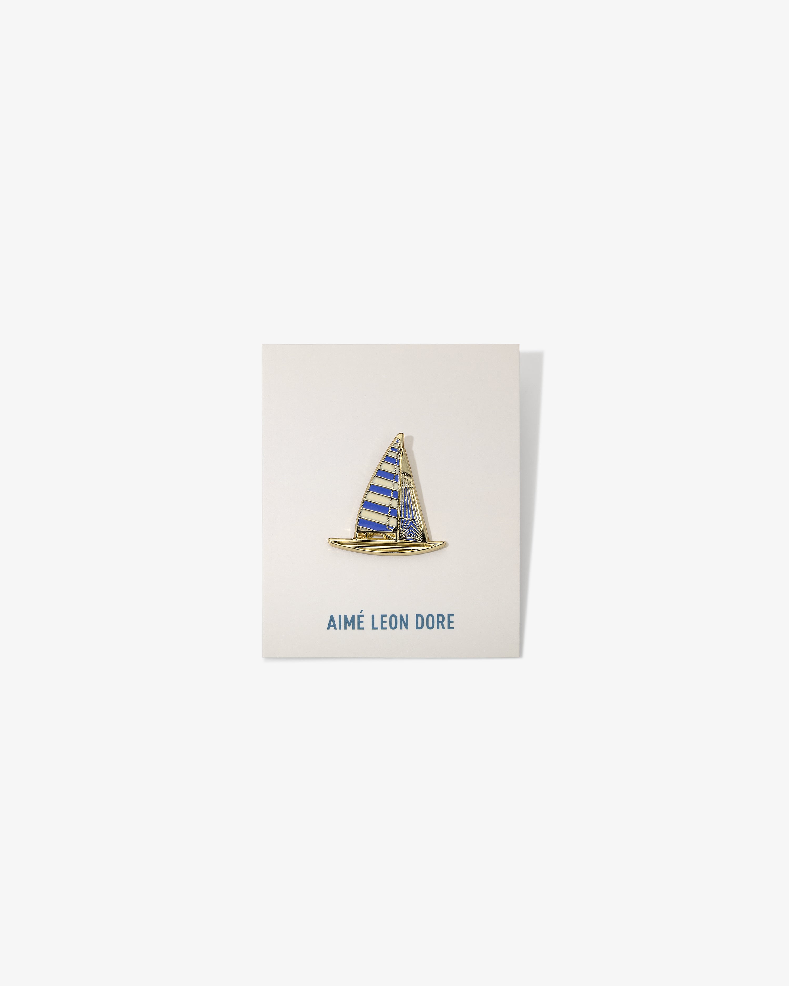 Graphic Pin featuring a sailboat with blue and yellow stripes, mounted on an AIMÉ LEON DORE card.