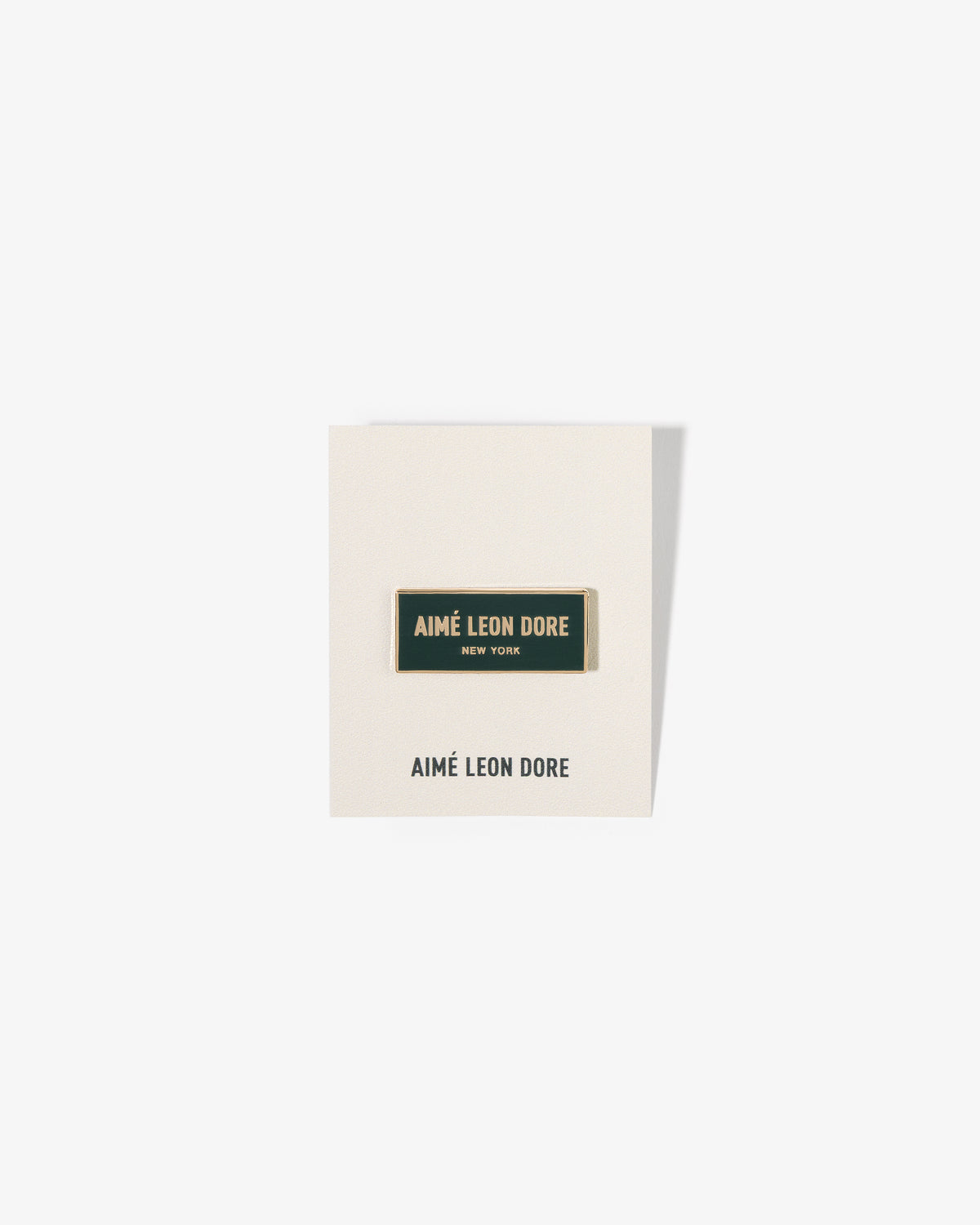 The Graphic Pin is a gold-outlined enamel pin on a white card with AIMÉ LEON DORE NEW YORK printed on it.